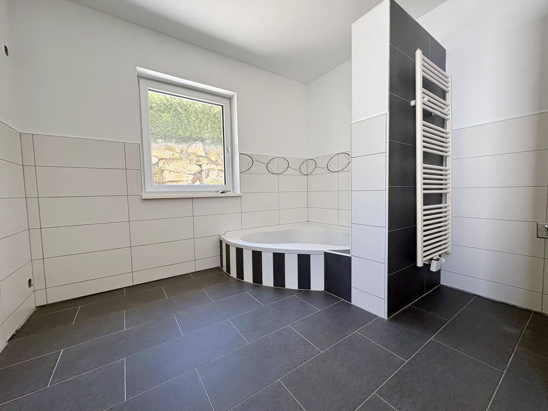 Modernes Badezimmer mit Eckbadewanne, dunklen Fliesen und beheiztem Handtuchhalter.