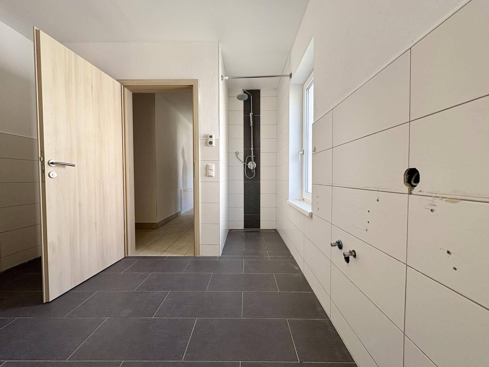 Geräumiges Badezimmer mit Duschbereich, dunklen Fliesen und Fenster.