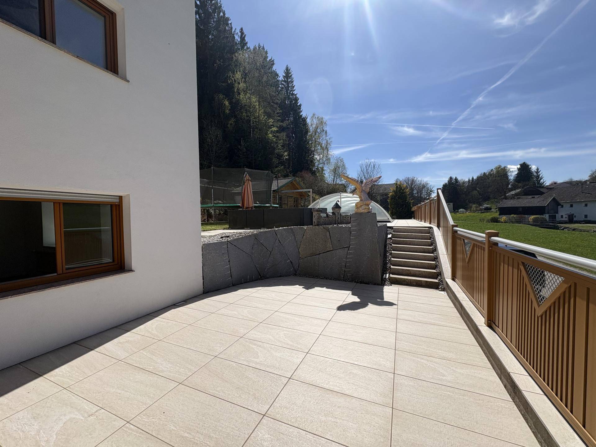 Sonniger Terrassenbereich neben dem Haus mit Treppe zum oberen Garten und Blick ins Grüne.