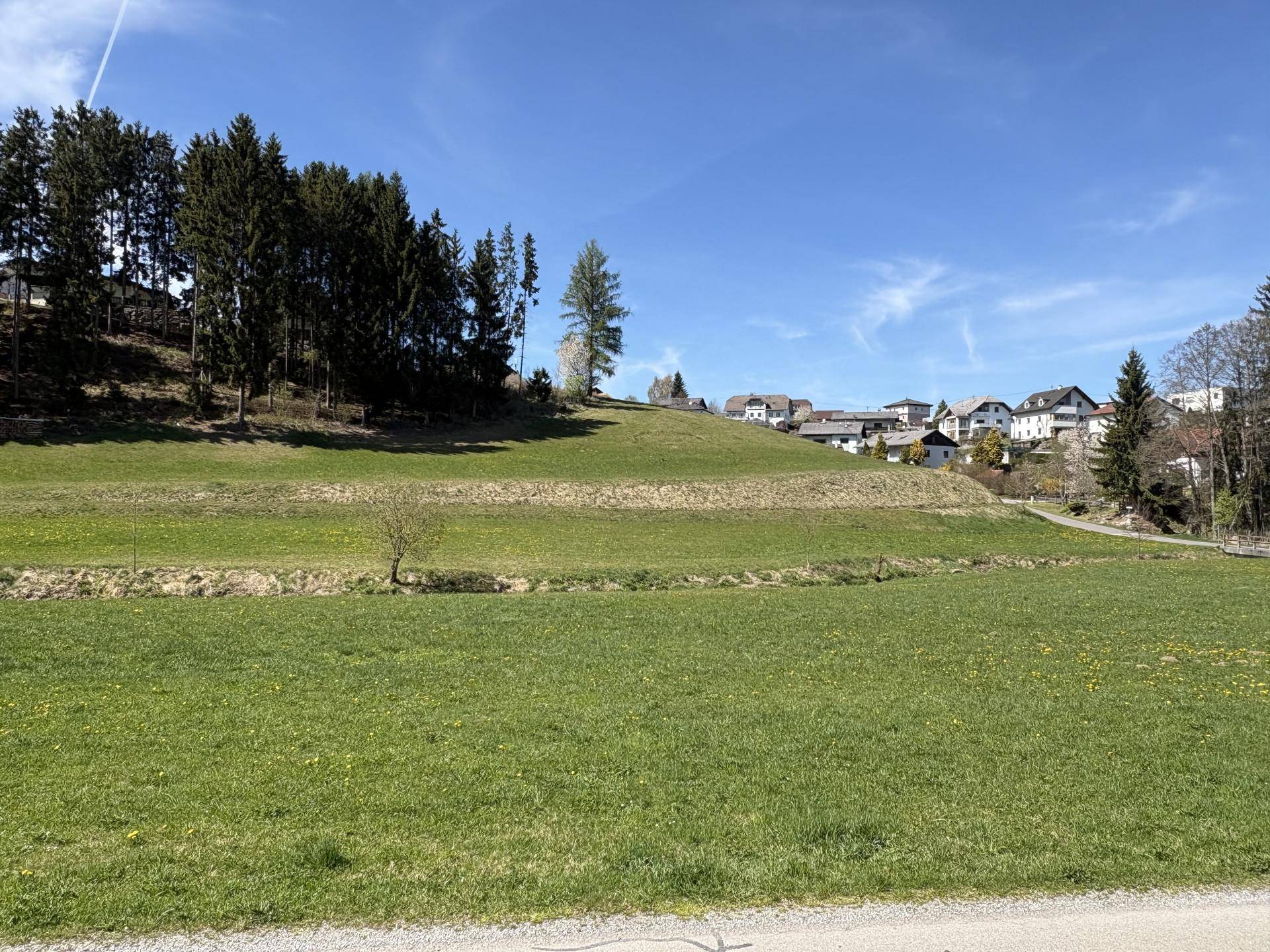Weitläufige grüne Landschaft mit sanften Hügeln und Häusern in der Ferne.