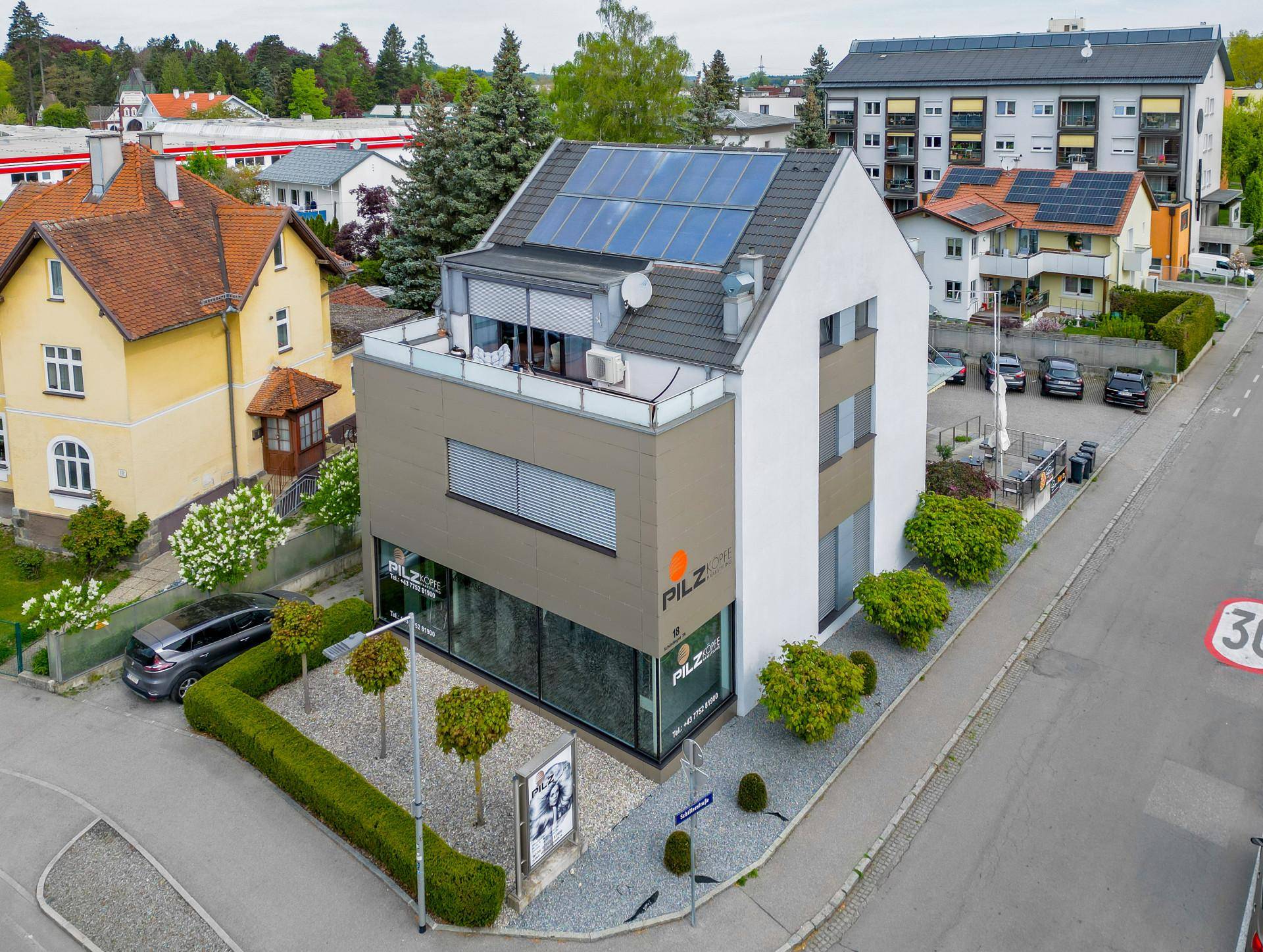 Luftaufnahme des modernen Gebäudes mit Photovoltaikanlage auf dem Dach und einer kleinen Dachterrasse.