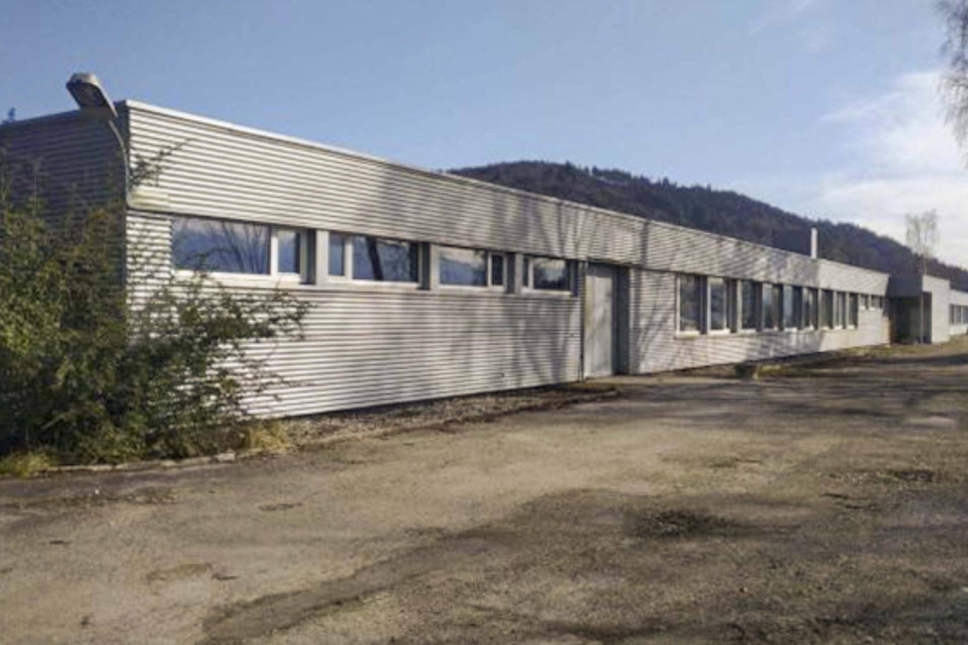 Langes Gewerbegebäude mit Wellblechfassade und zahlreichen Fenstern, umgeben von einer Zufahrt.