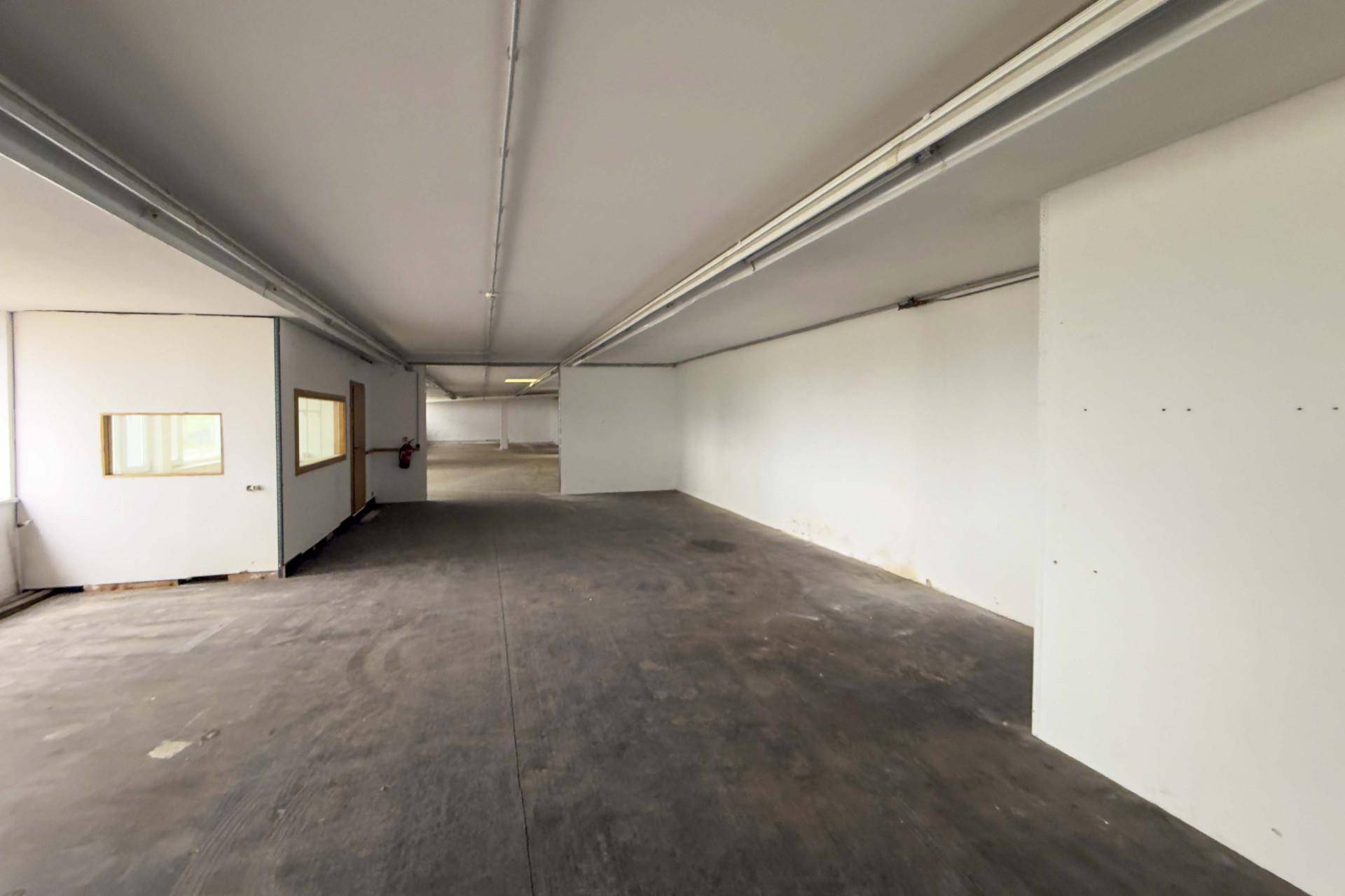 Langer, leerer Gewerberaum mit weißen Wänden und Betonboden, ideal für flexible Nutzung und Gestaltung.