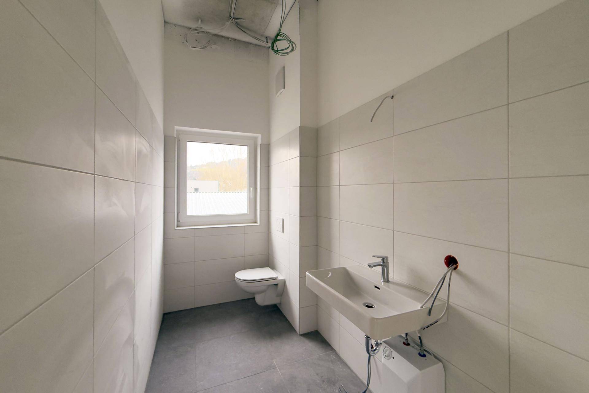 Modern gefliestes Badezimmer mit Waschbecken, Toilette und Fenster, noch im Bau.