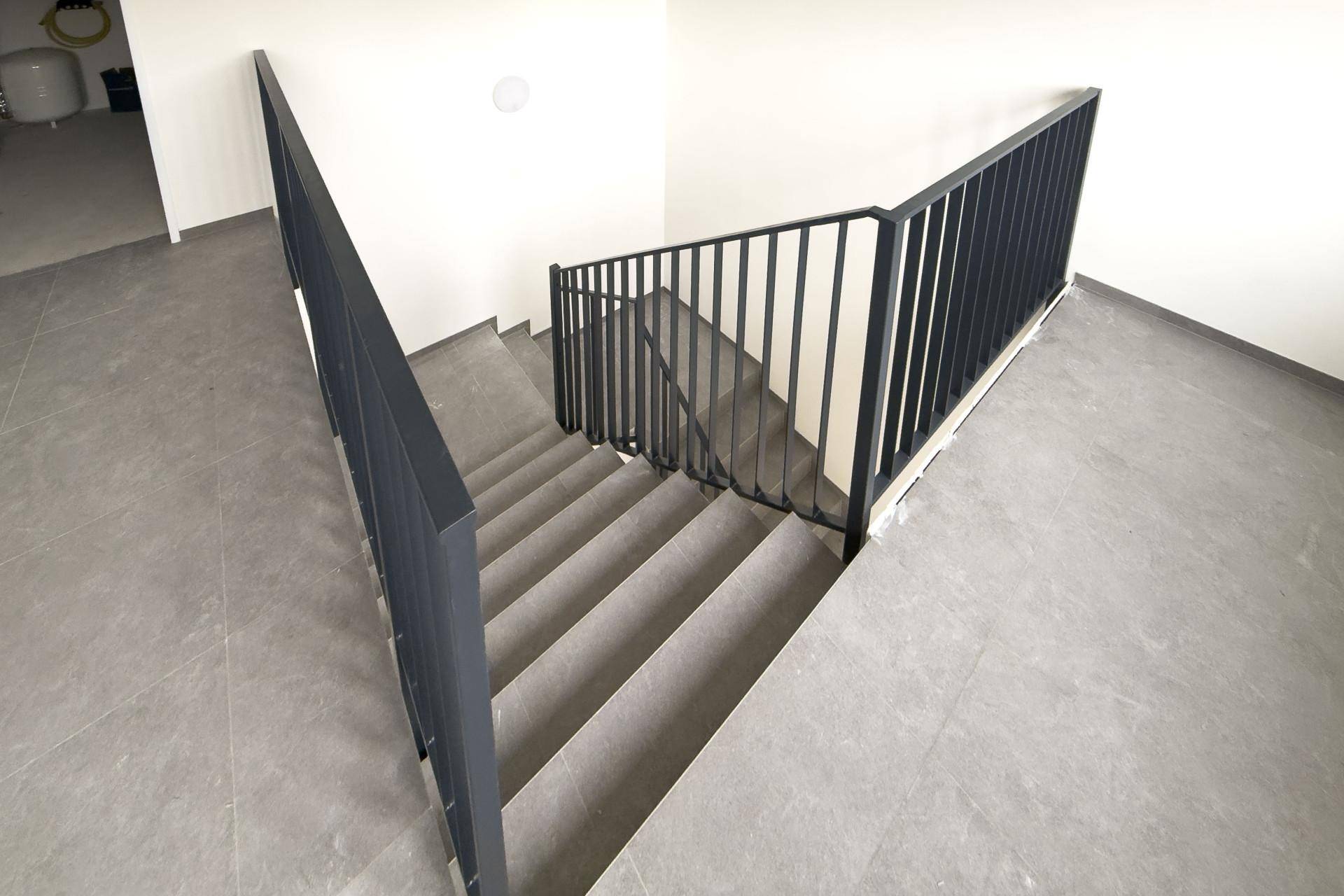 Moderner Treppenaufgang mit dunklem Metallgeländer und Fliesenboden.