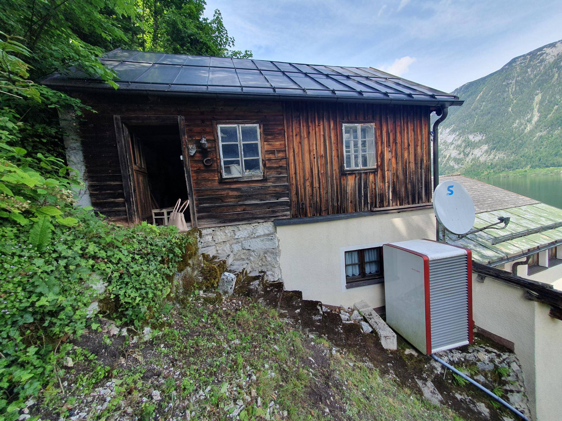 Rustikales Holzhaus am Hang mit Solarpaneelen auf dem Dach und einer Wärmepumpe im Freien.
