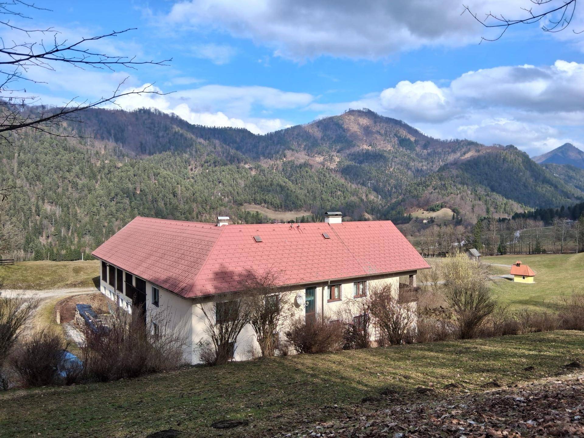 Traditionelles Gebäude mit rotem Dach und weitem Blick auf die umliegende Berglandschaft unter bewölktem Himmel.