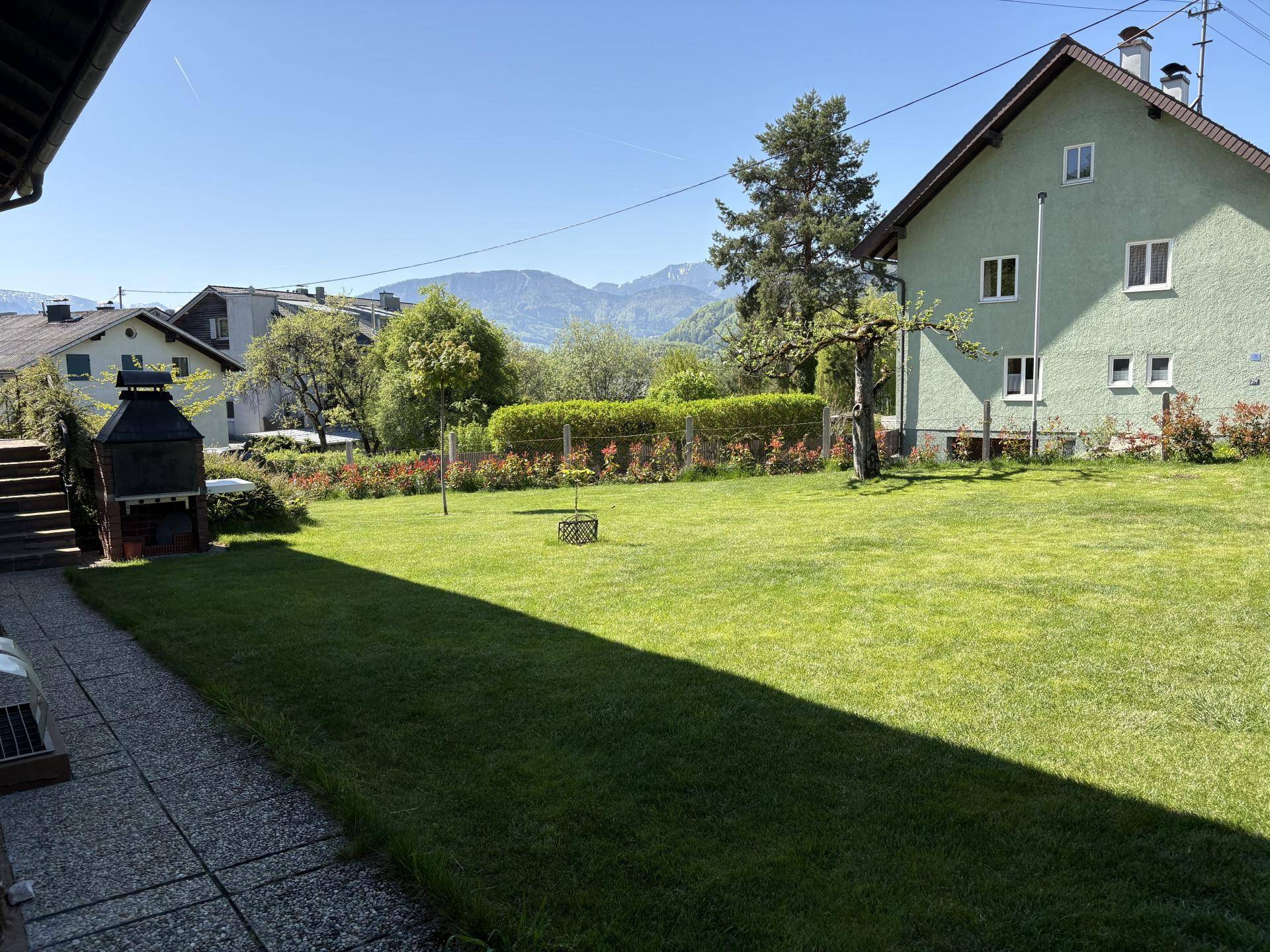 Großer, gepflegter Rasenbereich mit Grillplatz und Blick auf die umliegende Berglandschaft.