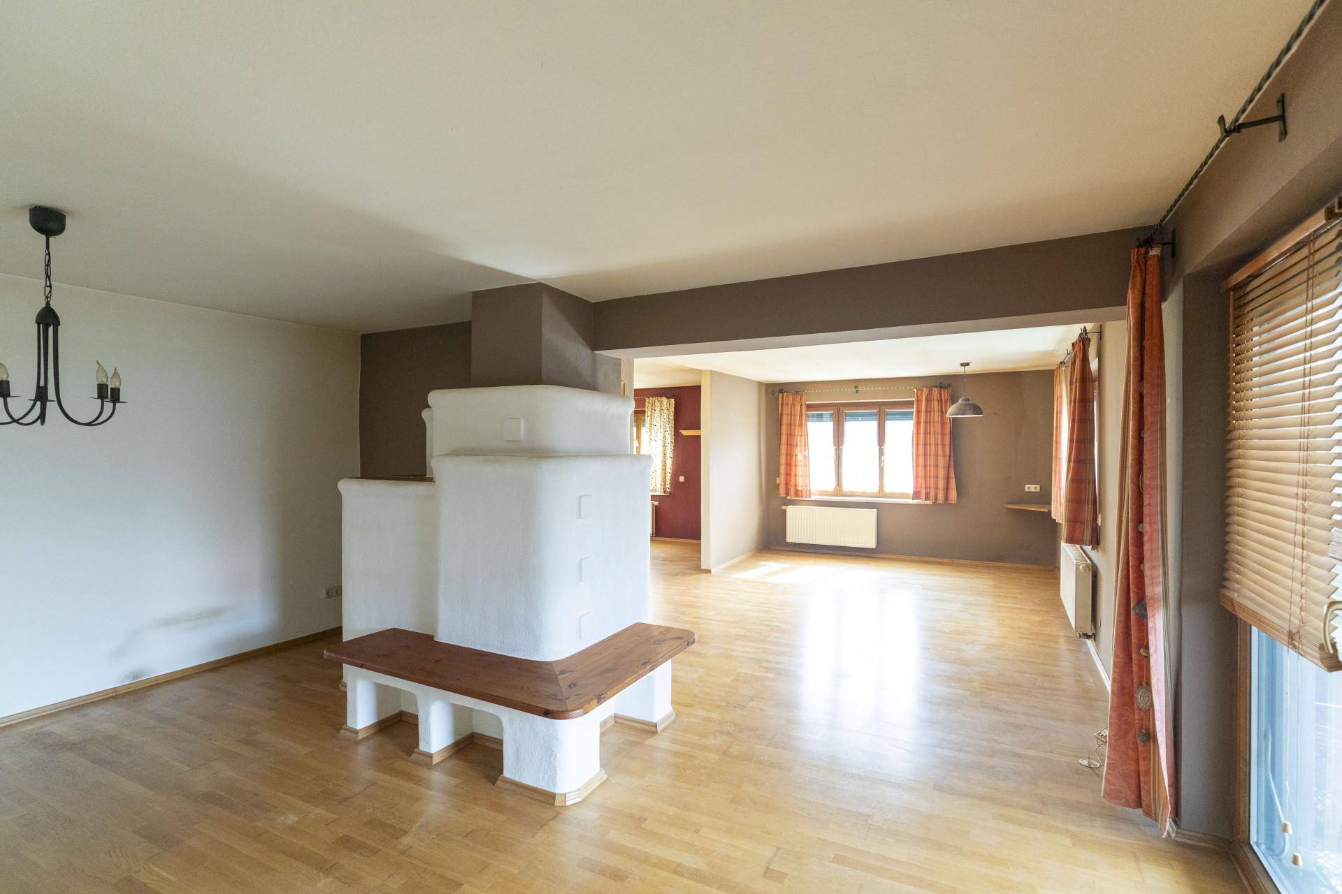Geräumiges Wohnzimmer mit Holzboden und traditionellem Kachelofen als zentralem Element.