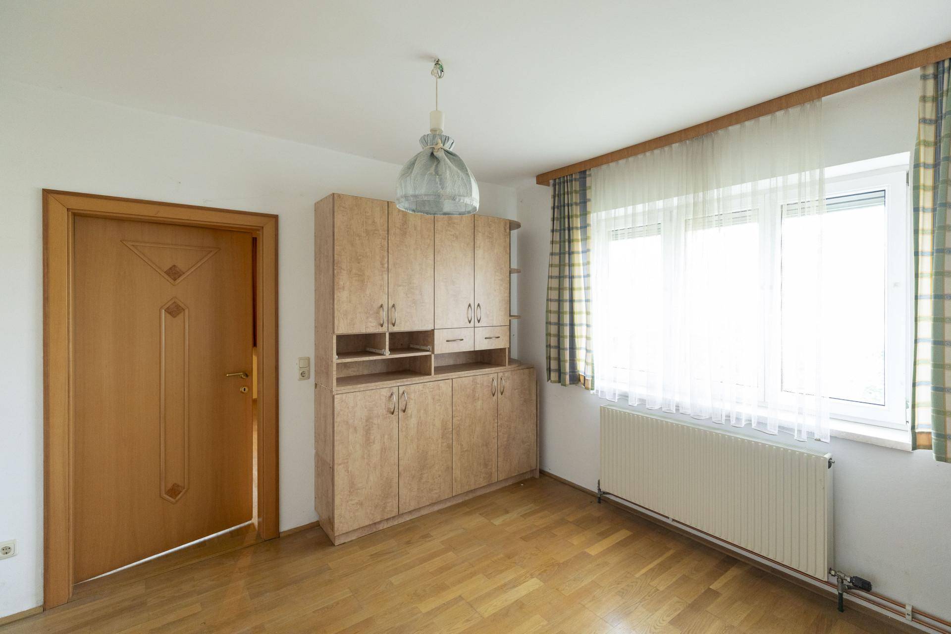 Schlafzimmer mit Holzboden, großem Kleiderschrank und einem Fenster mit karierten Vorhängen.