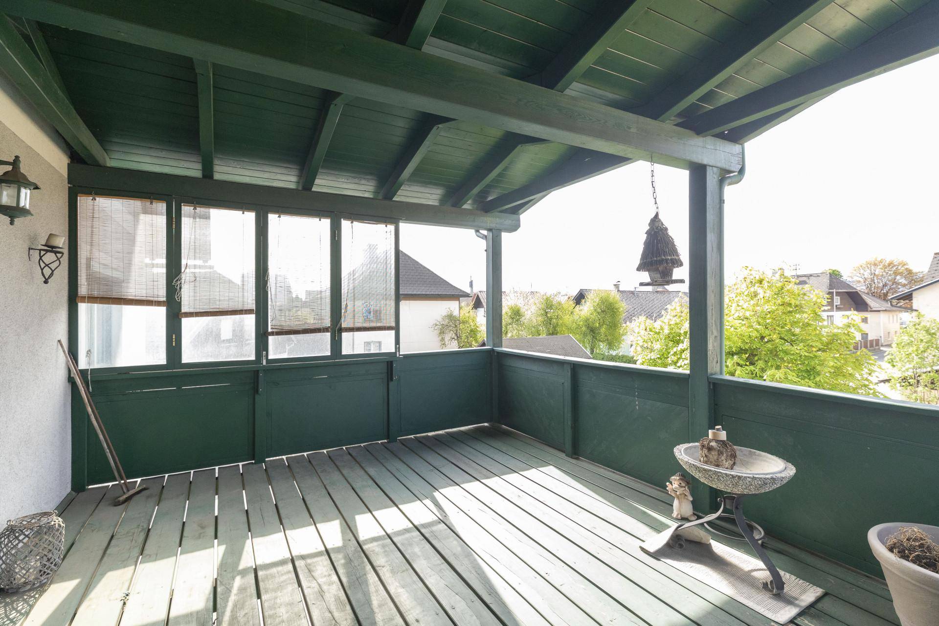 Überdachter Holzbalkon mit grüner Holzverkleidung und Blick auf die Umgebung.