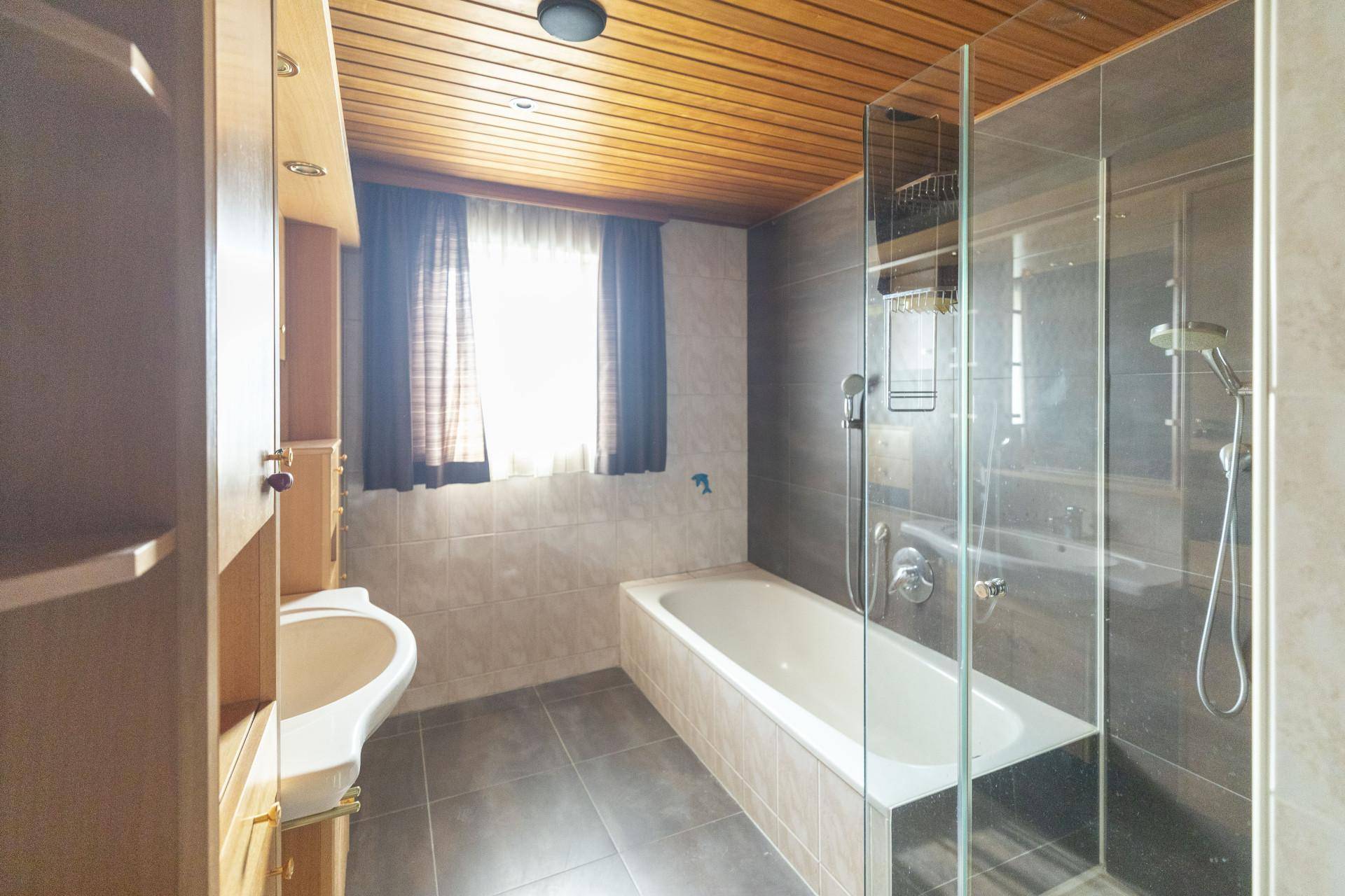 Badezimmer mit Badewanne, Dusche, Waschbecken und Holzdecke, ausgestattet mit Fliesen.