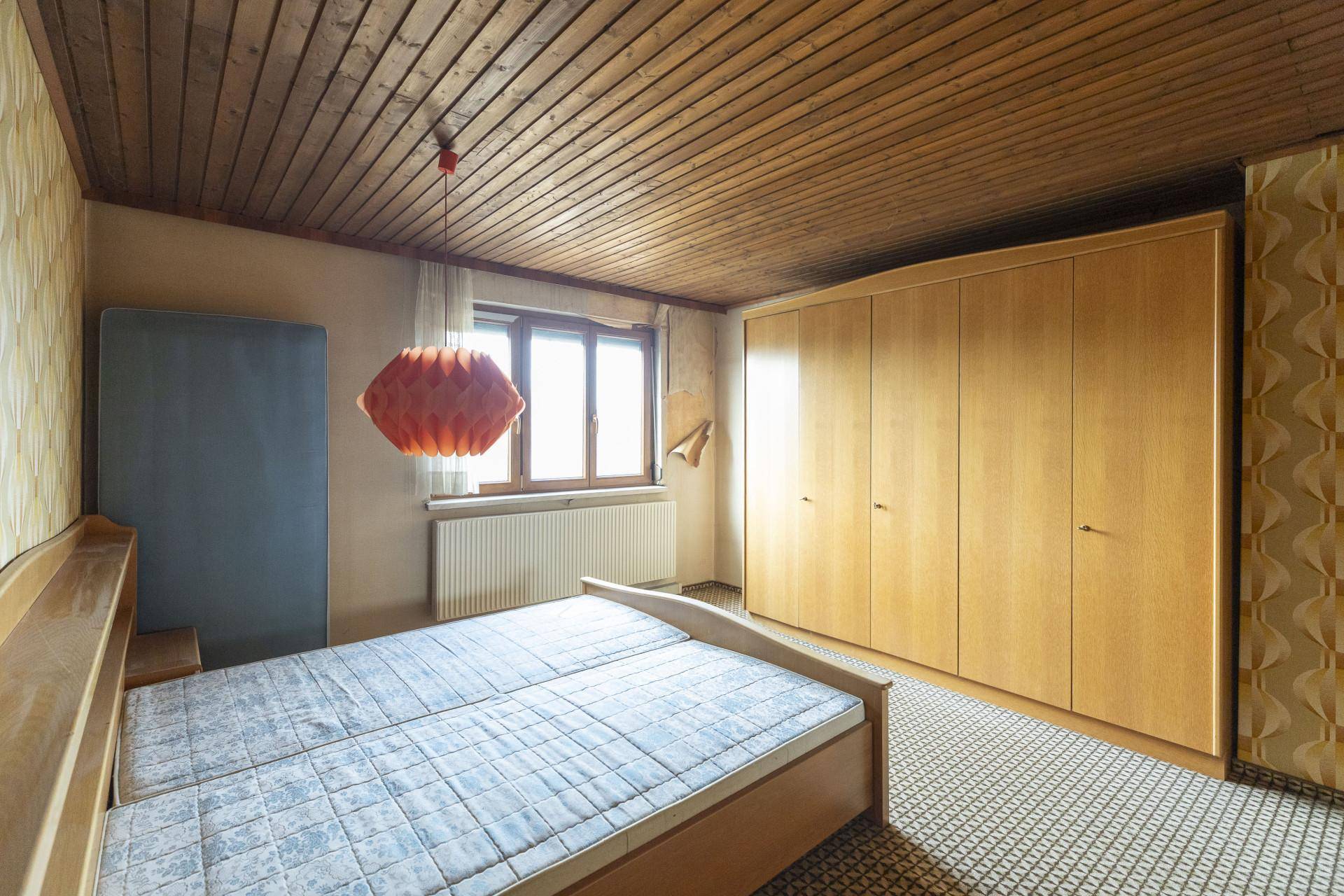 Schlafzimmer mit Holzbett, großem Kleiderschrank und Holzdecke, dekoriert mit Tapeten.