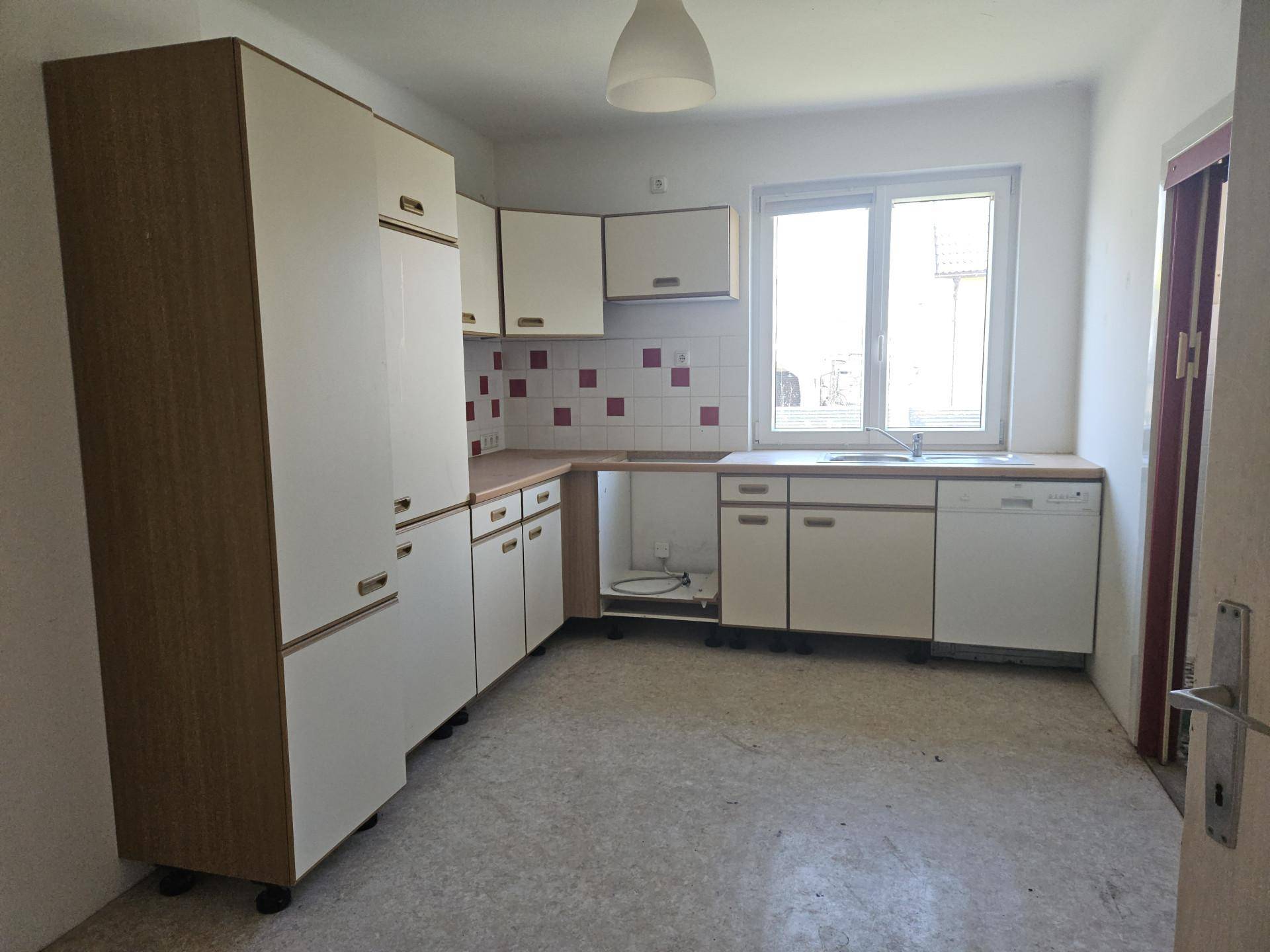 Ältere Einbauküche mit weißen Schränken, Holzoptik-Elementen und Fliesenrückwand, renovierungsbedürftig.