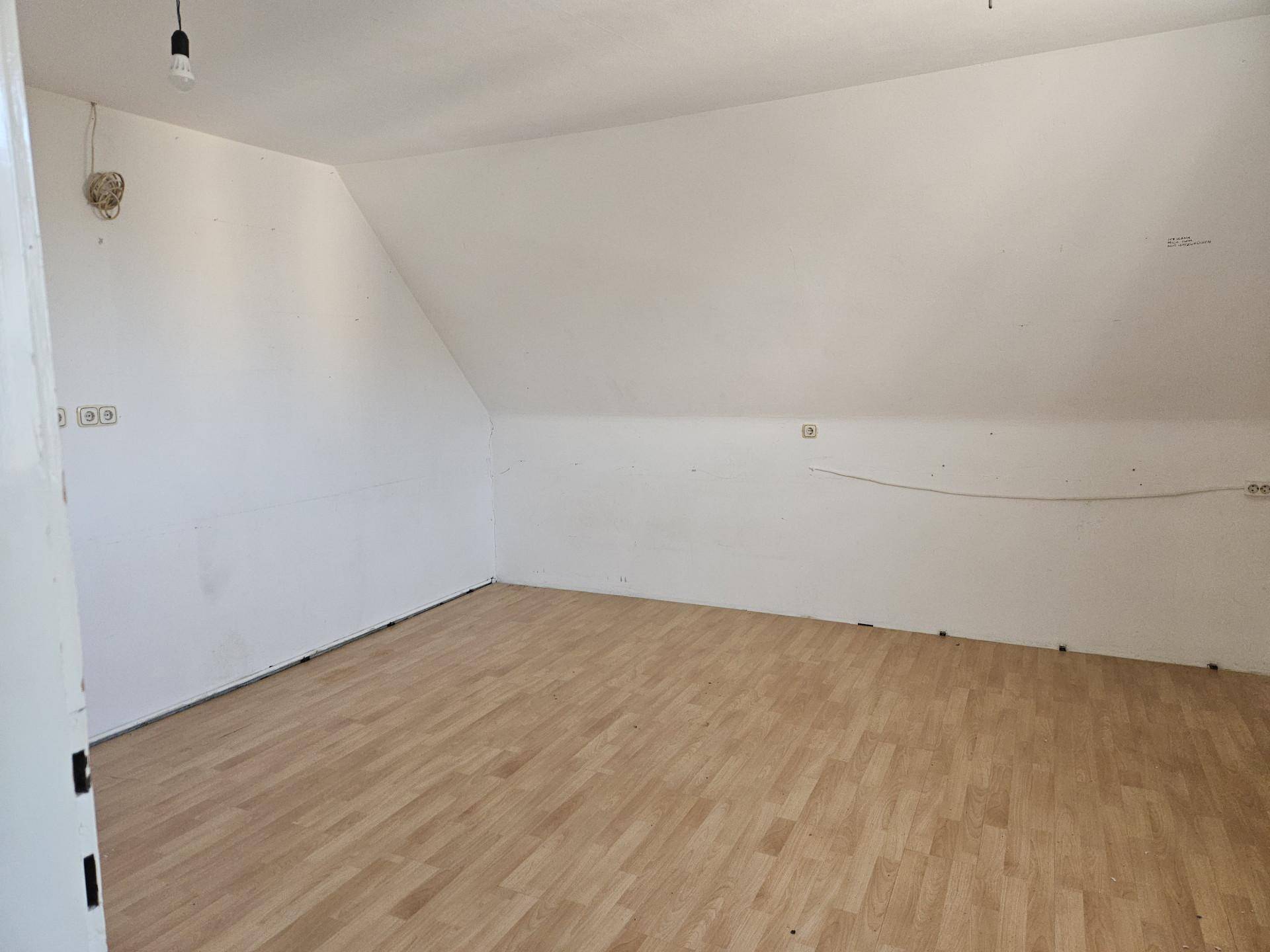 Dachgeschosszimmer mit schrägen Wänden und Laminatboden, bereit für individuelle Gestaltung.