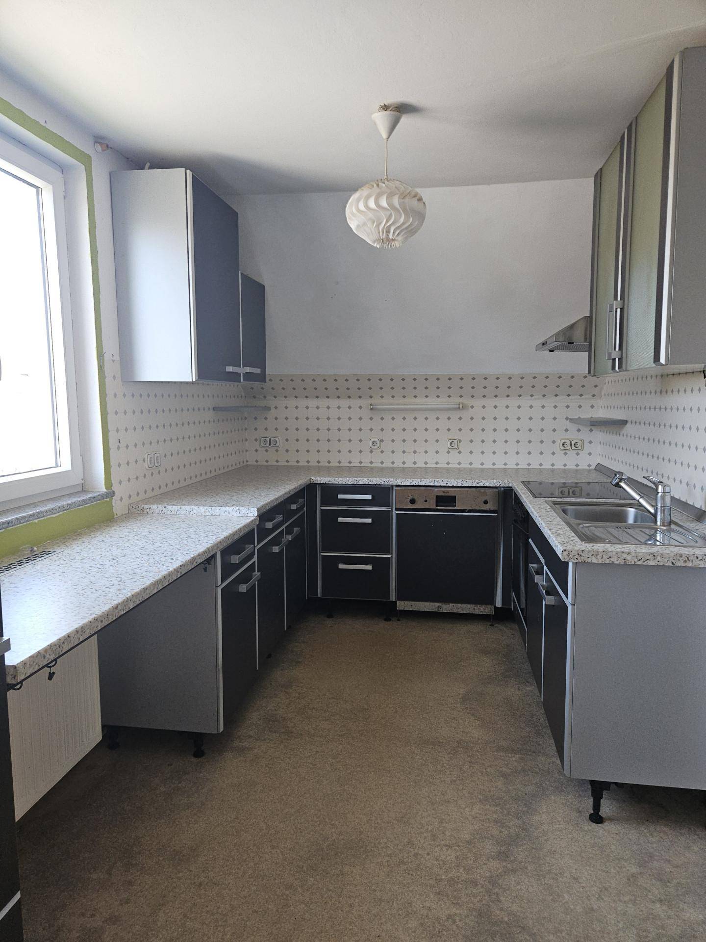 Funktionale Küche mit grauen Schränken, gemusterten Fliesen und Fenster für Tageslicht.