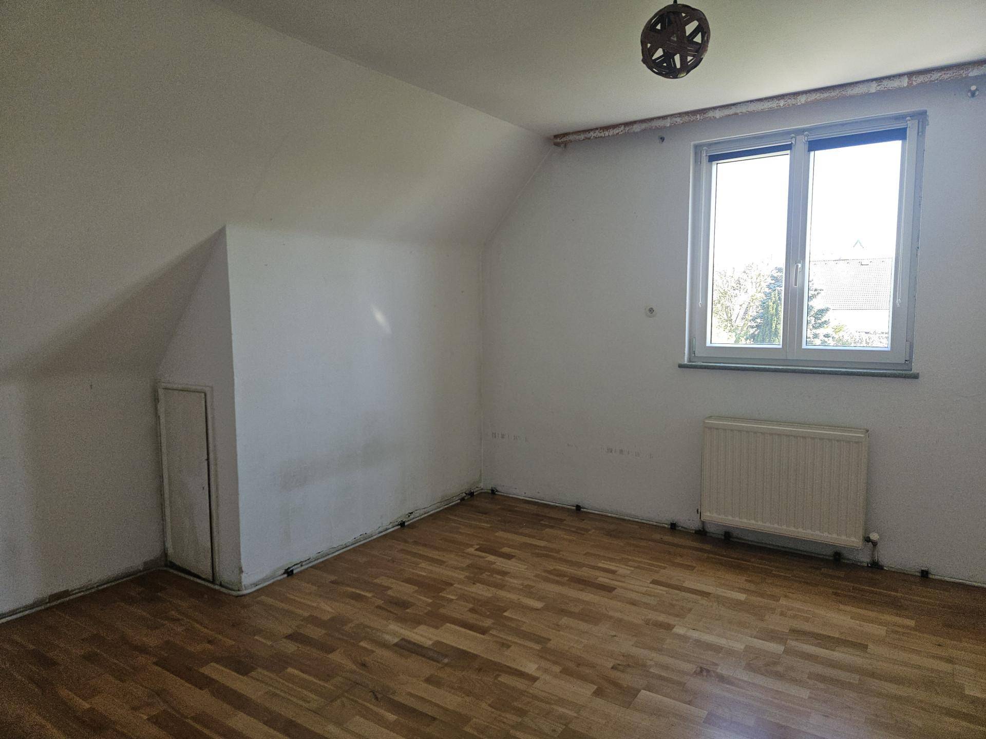 Helles Schlafzimmer im Dachgeschoss mit Laminatboden, Heizkörper und Fenster.