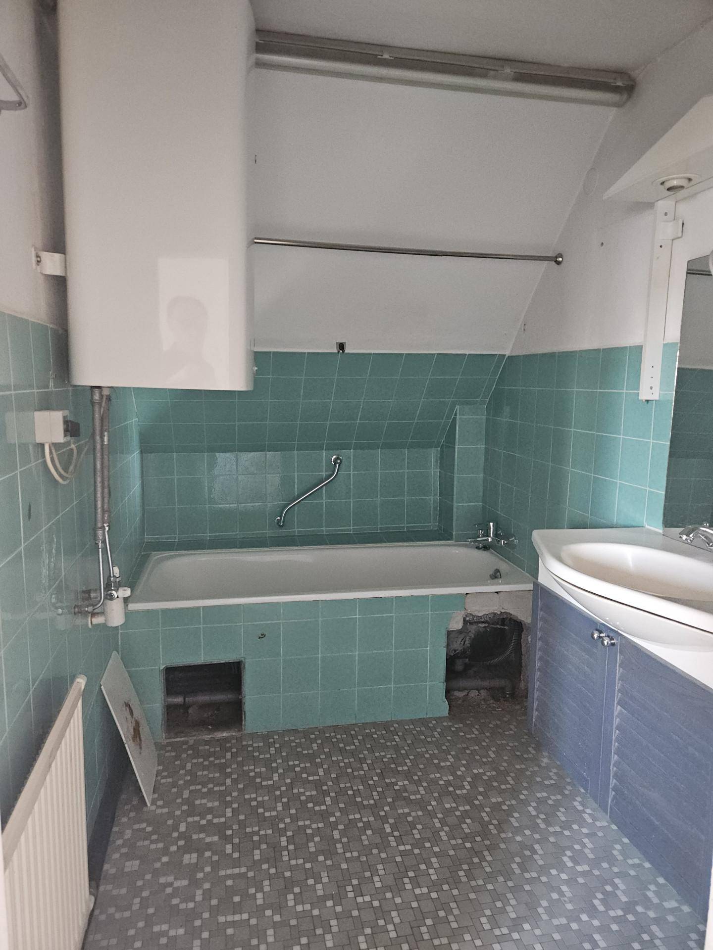 Badezimmer mit mintgrünen Fliesen, Badewanne und Waschbecken, renovierungsbedürftig.