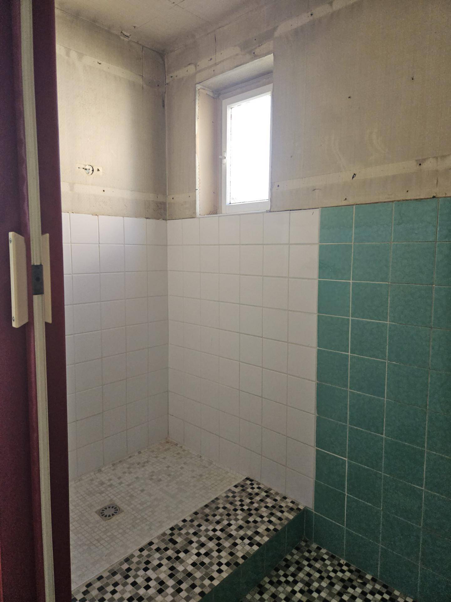 Duschbereich mit weißen und mintgrünen Fliesen sowie einem kleinen Fenster.