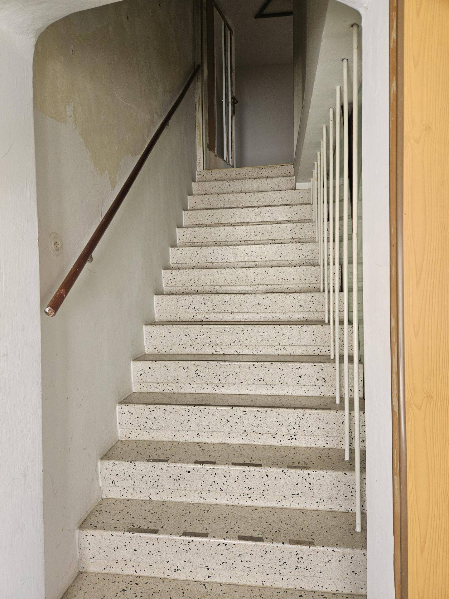 Treppenhaus mit Terrazzo-Stufen und schlichtem Geländer, das in die oberen Stockwerke führt.