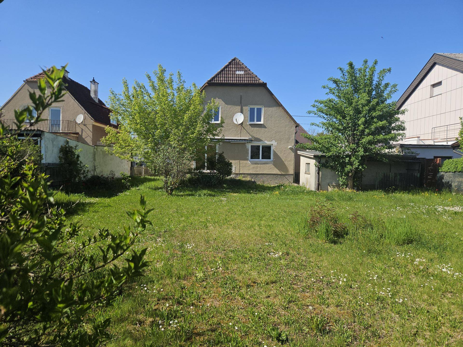 Rückansicht des Hauses mit großem Garten und viel Grünfläche unter strahlend blauem Himmel.