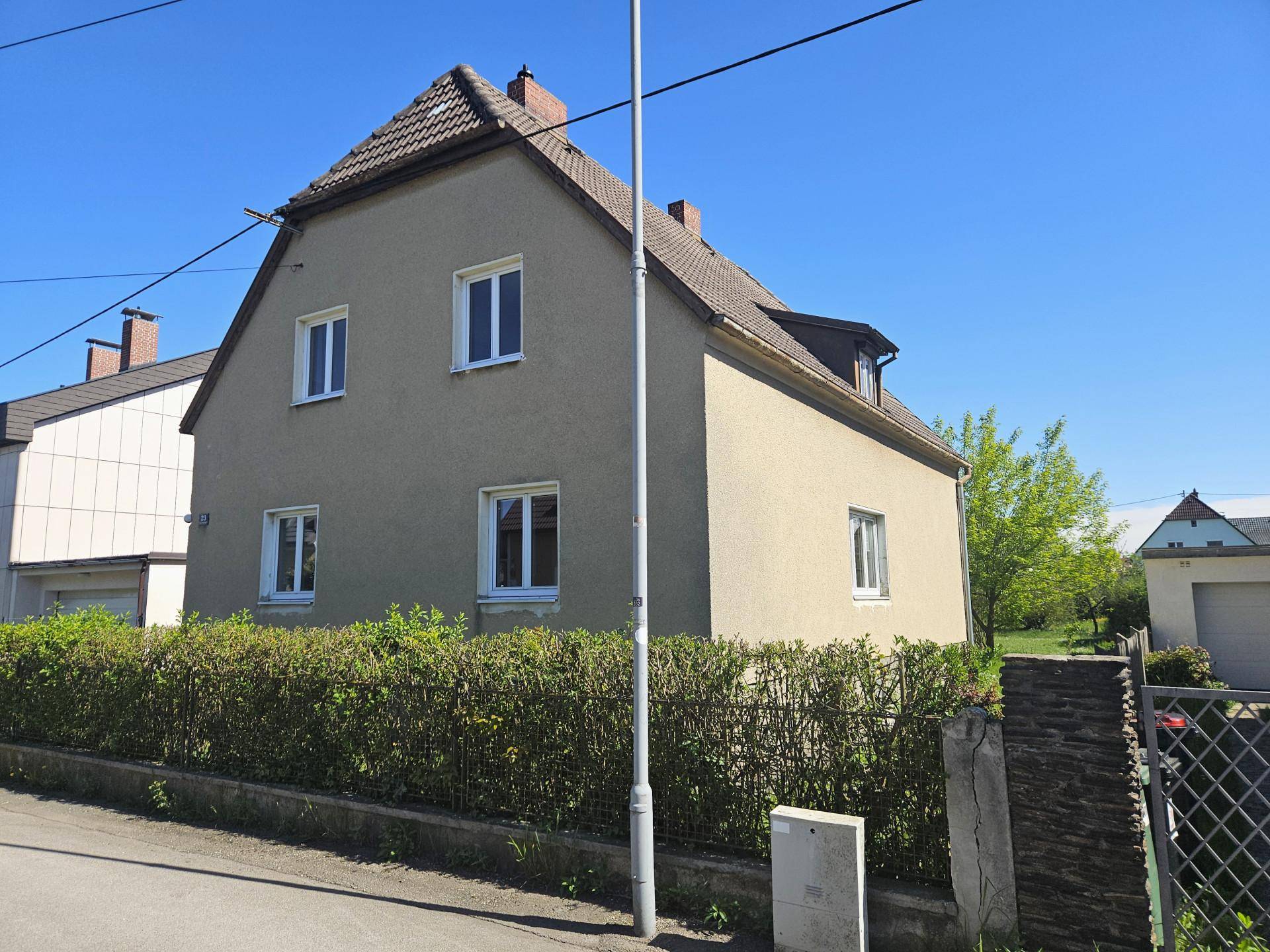 Seitenansicht des Hauses mit Satteldach, Putzfassade und gepflegter Hecke im Vorgarten.