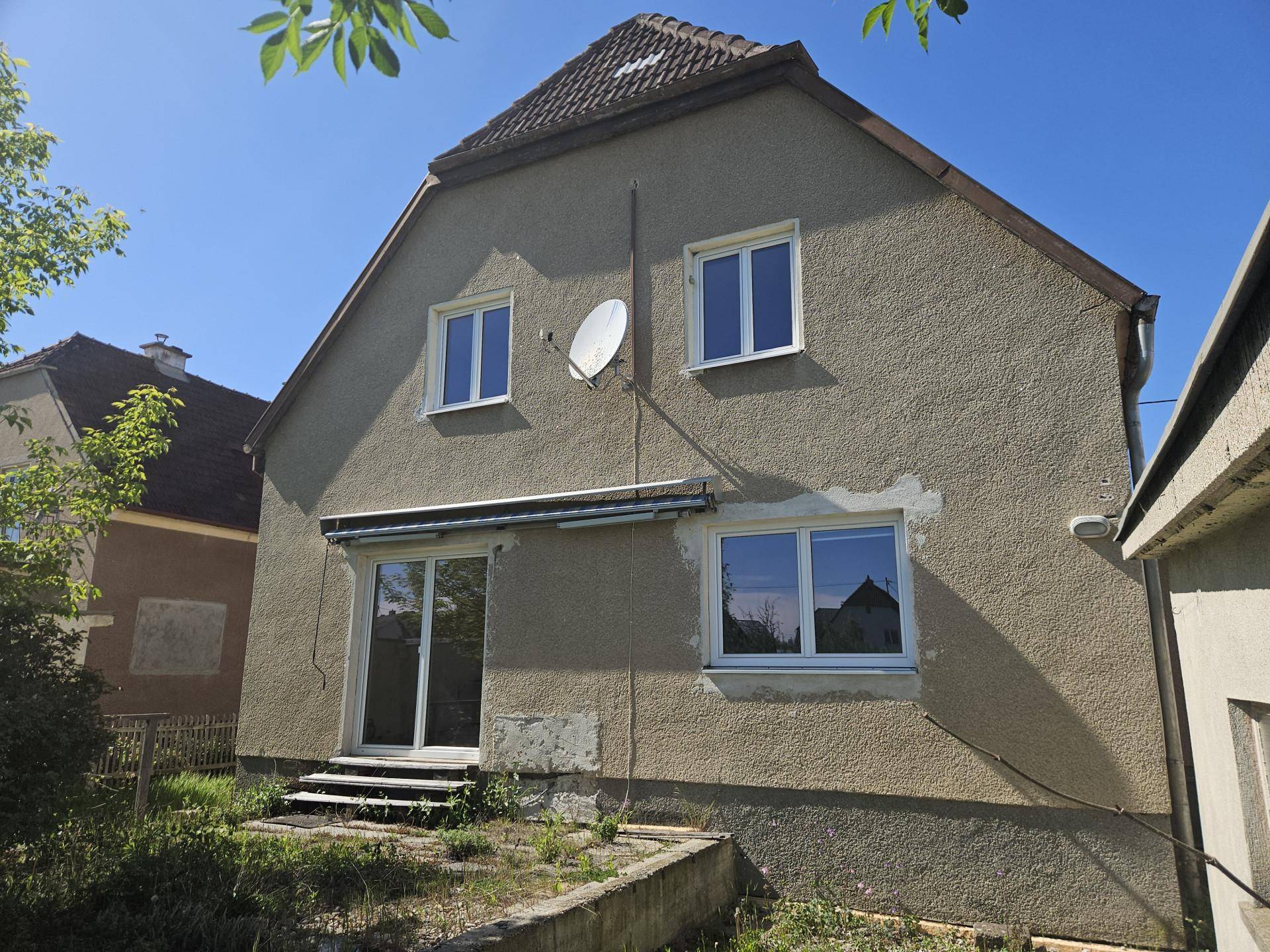 Rückseite des Hauses mit Putzfassade, Fenstern und Zugang zum Gartenbereich.