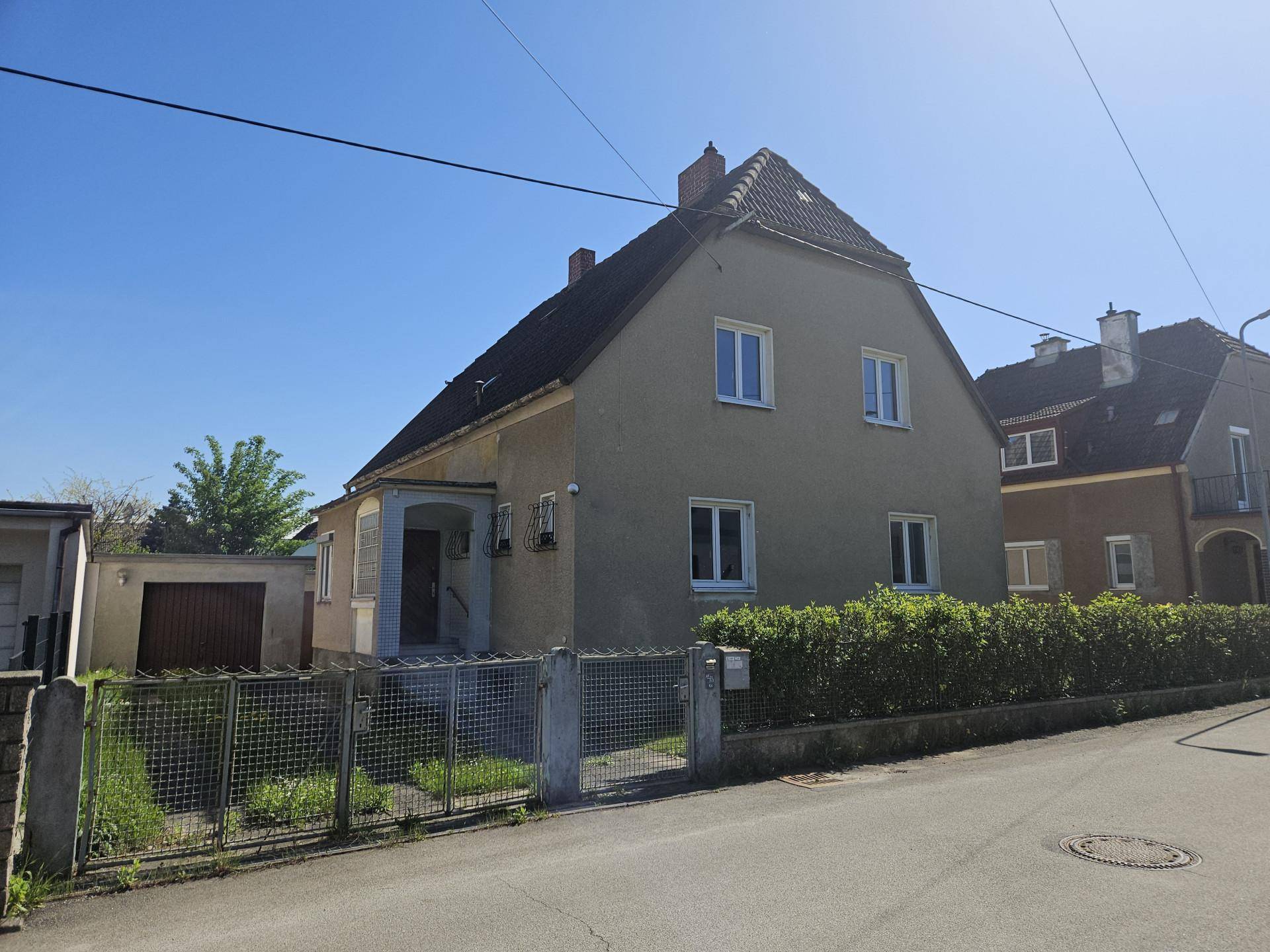 Einfamilienhaus mit Satteldach, grüner Fassade und gepflegtem Vorgarten, umgeben von einer Hecke.