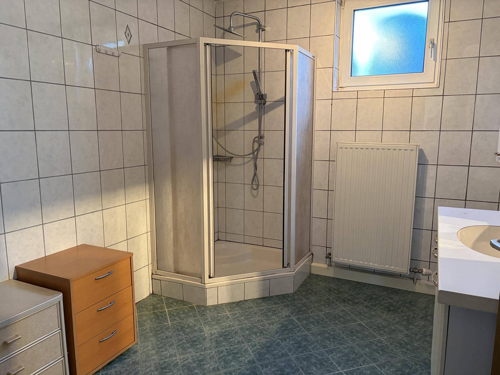 Badezimmer mit Duschkabine, Fliesen an Wänden und Boden, sowie einem Fenster.