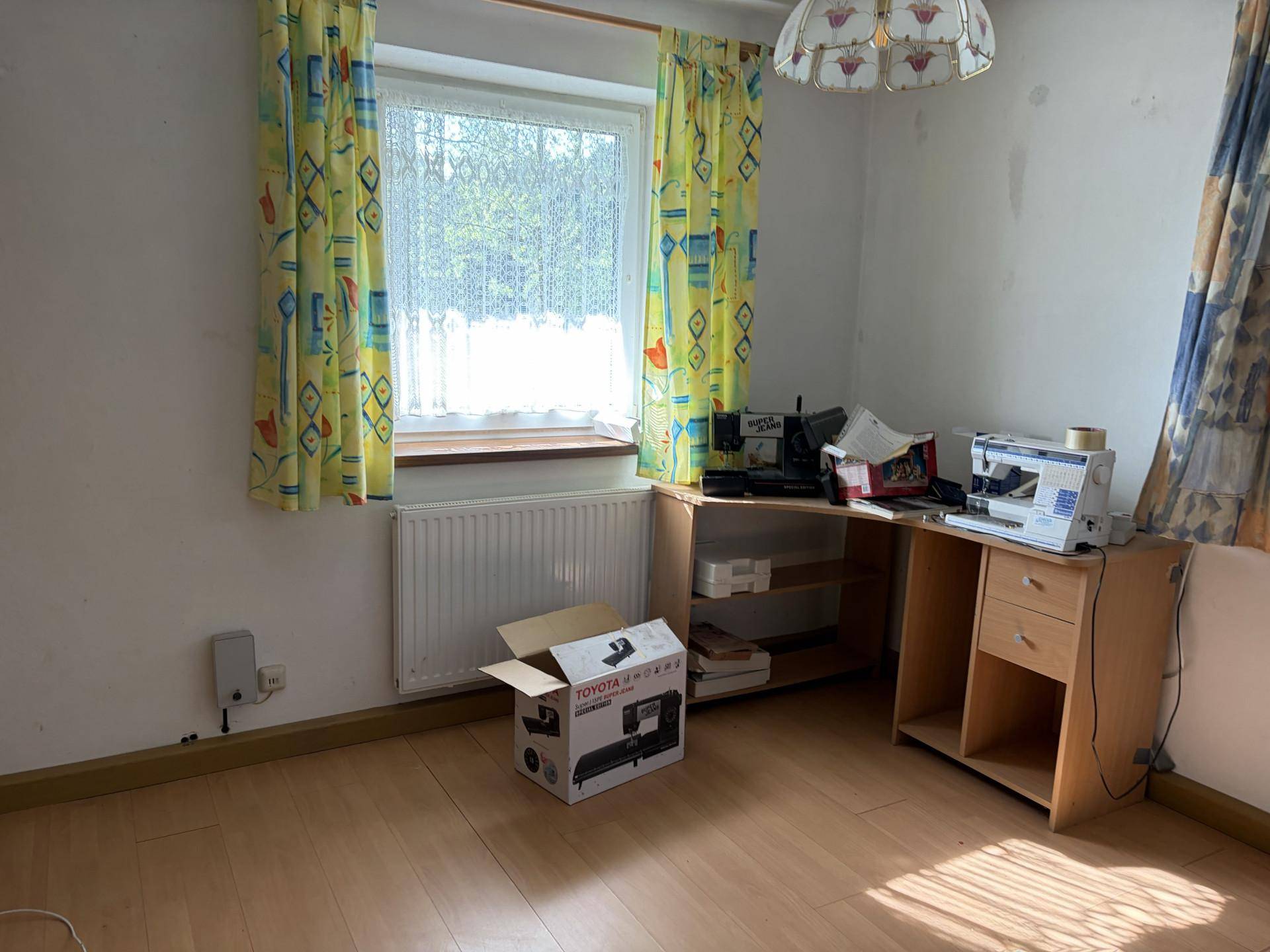 Arbeitszimmer mit Laminatboden und Fenster, ausgestattet mit Nähmaschinen und Schreibtisch.