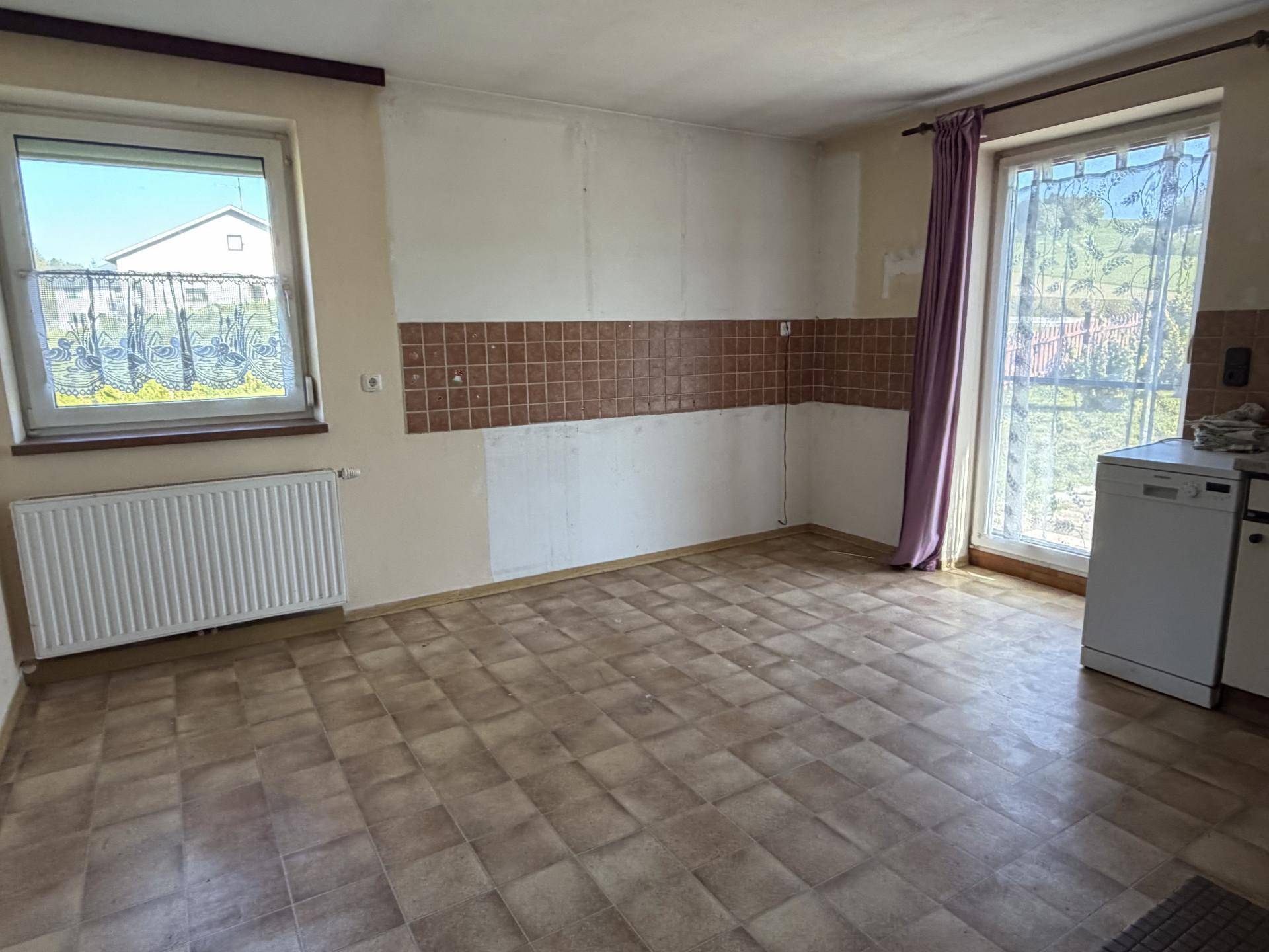 Geräumige Küche mit Fliesenboden und Fenster, bereit für eine neue Kücheneinrichtung.