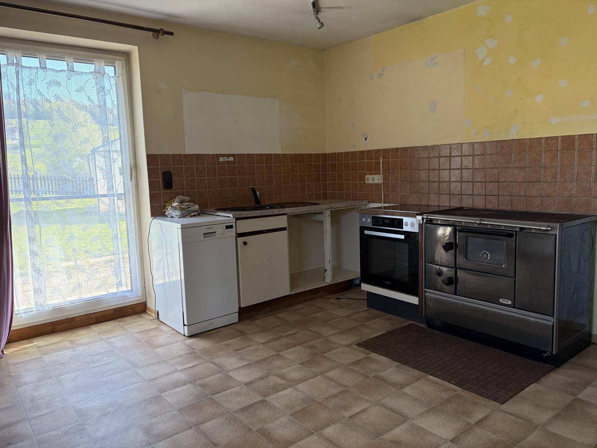 Küche mit Fliesenboden, Spülmaschine und traditionellem Holzofen, renovierungsbedürftig.