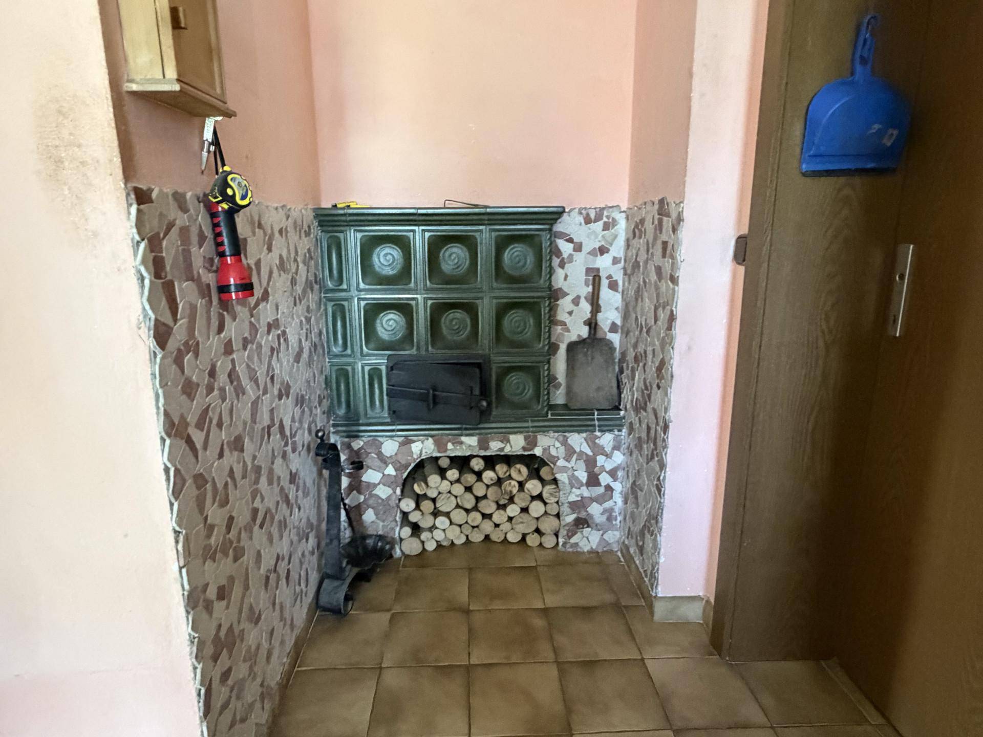Eingangsbereich mit traditionellem Kachelofen und Holzstapel, gefliestem Boden.