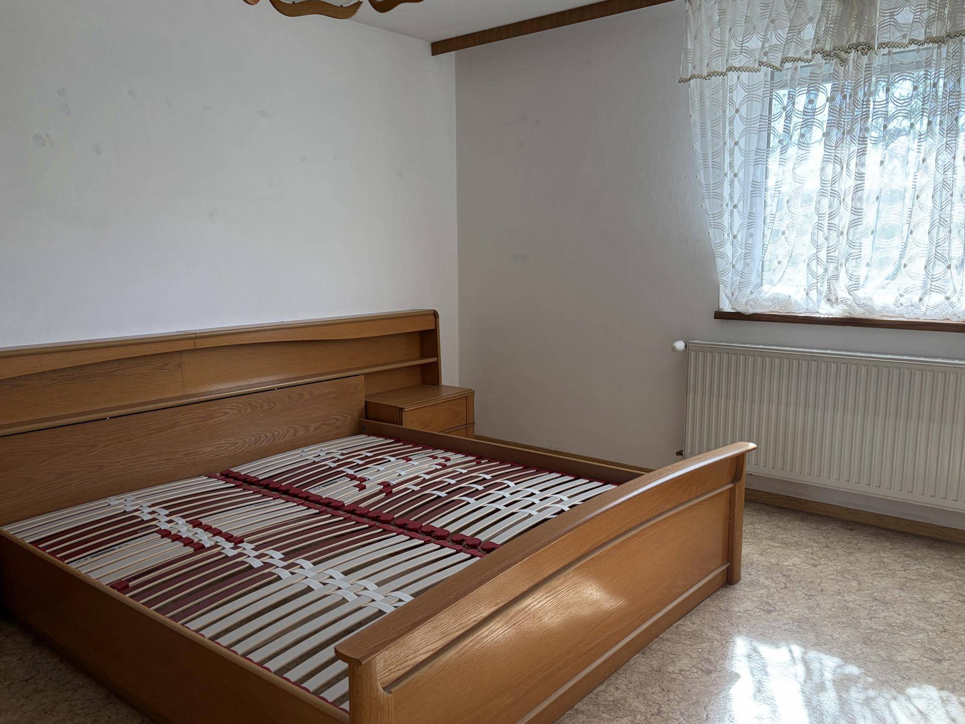 Schlafzimmer mit Holzbettrahmen und Fenster, das viel Tageslicht hereinlässt.