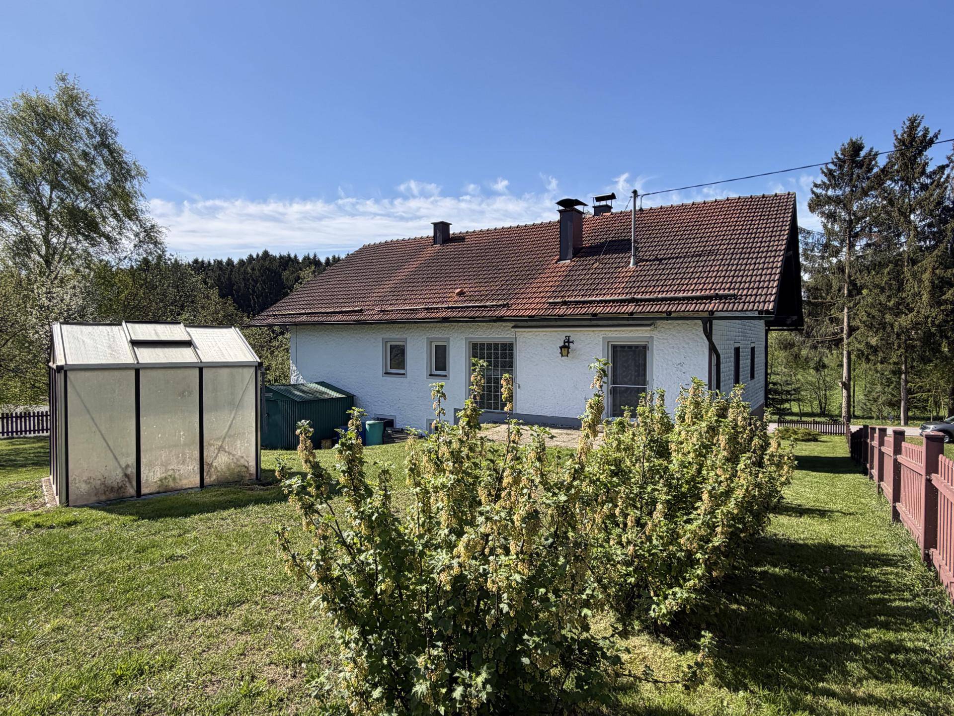 Hinterer Gartenbereich mit Gewächshaus, Beerensträuchern und Blick auf die Landschaft.