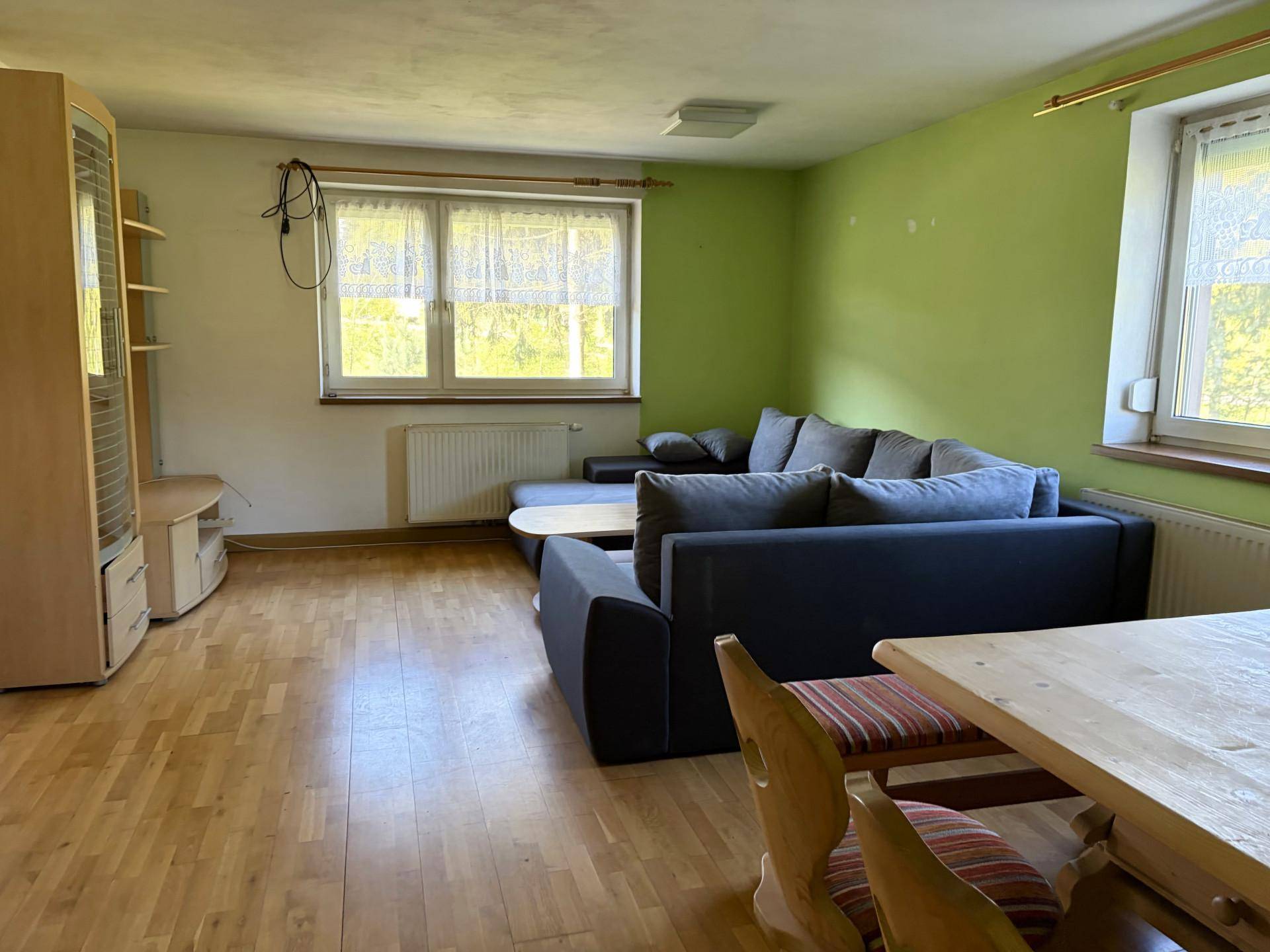 Wohnzimmer mit grün gestrichenen Wänden, Laminatboden und gemütlicher Sitzecke am Fenster.
