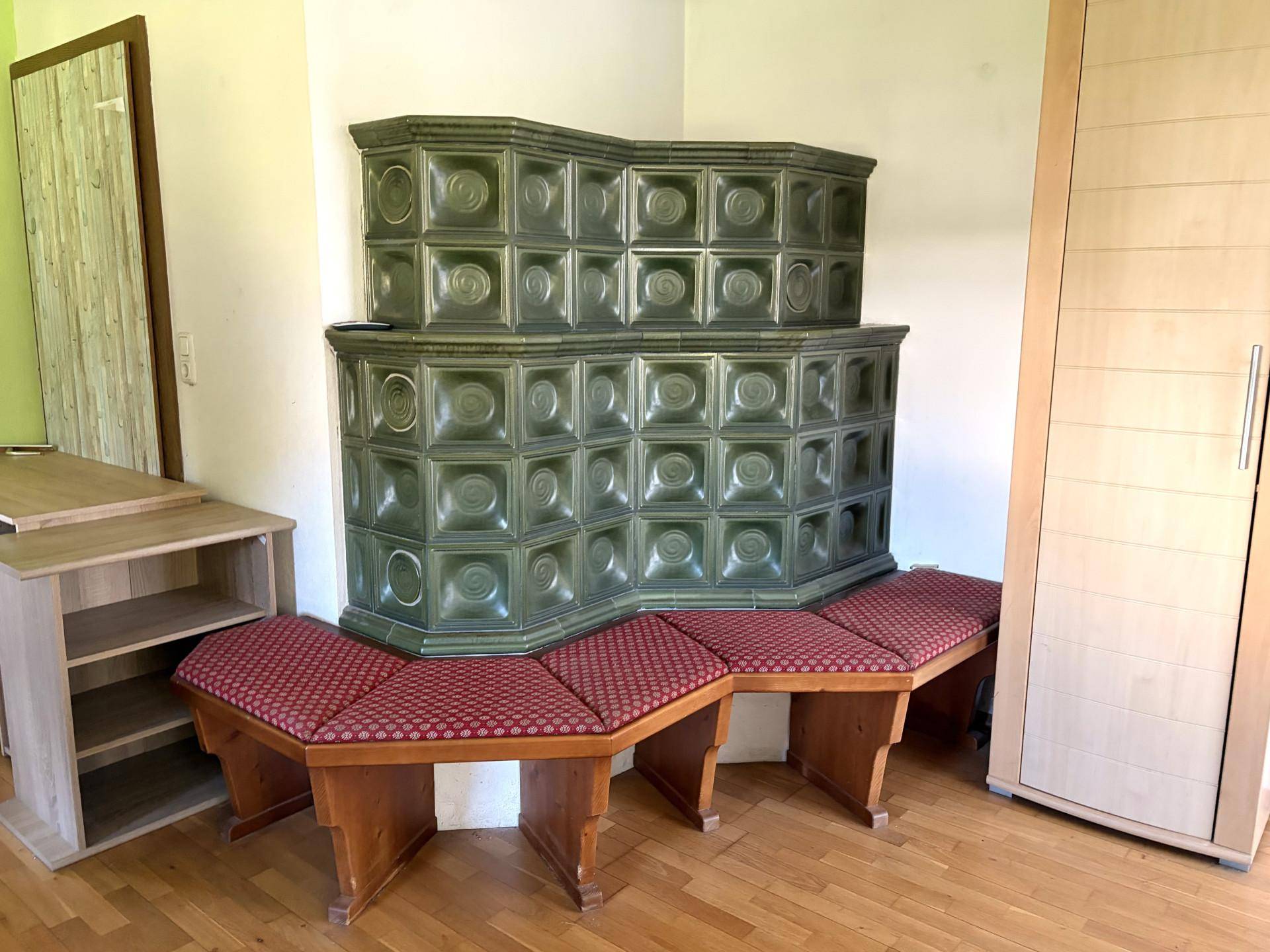 Traditioneller grüner Kachelofen mit Sitzbänken, ein zentrales Element im Wohnbereich.