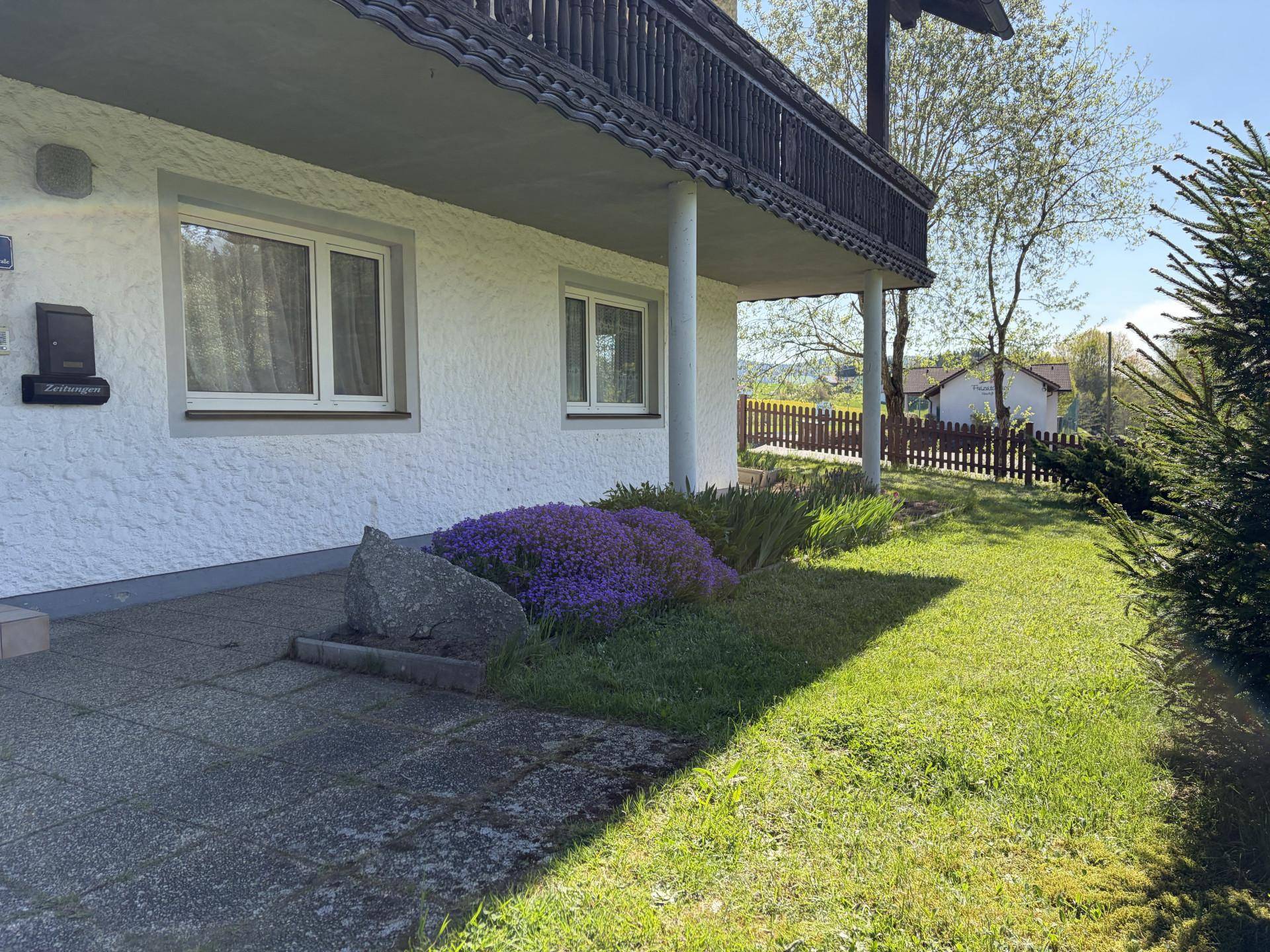 Vorgarten mit gepflegtem Rasen, Blumenbeet und Zugang zum Haus.