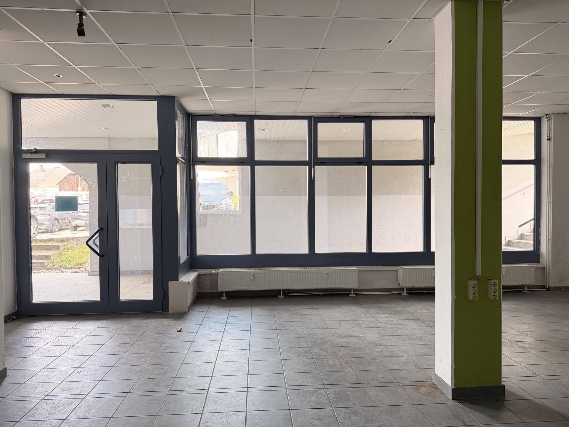 Eingangsbereich eines Gewerberaums mit großen Glasfenstern und einer Glastür, die viel Tageslicht hereinlassen.