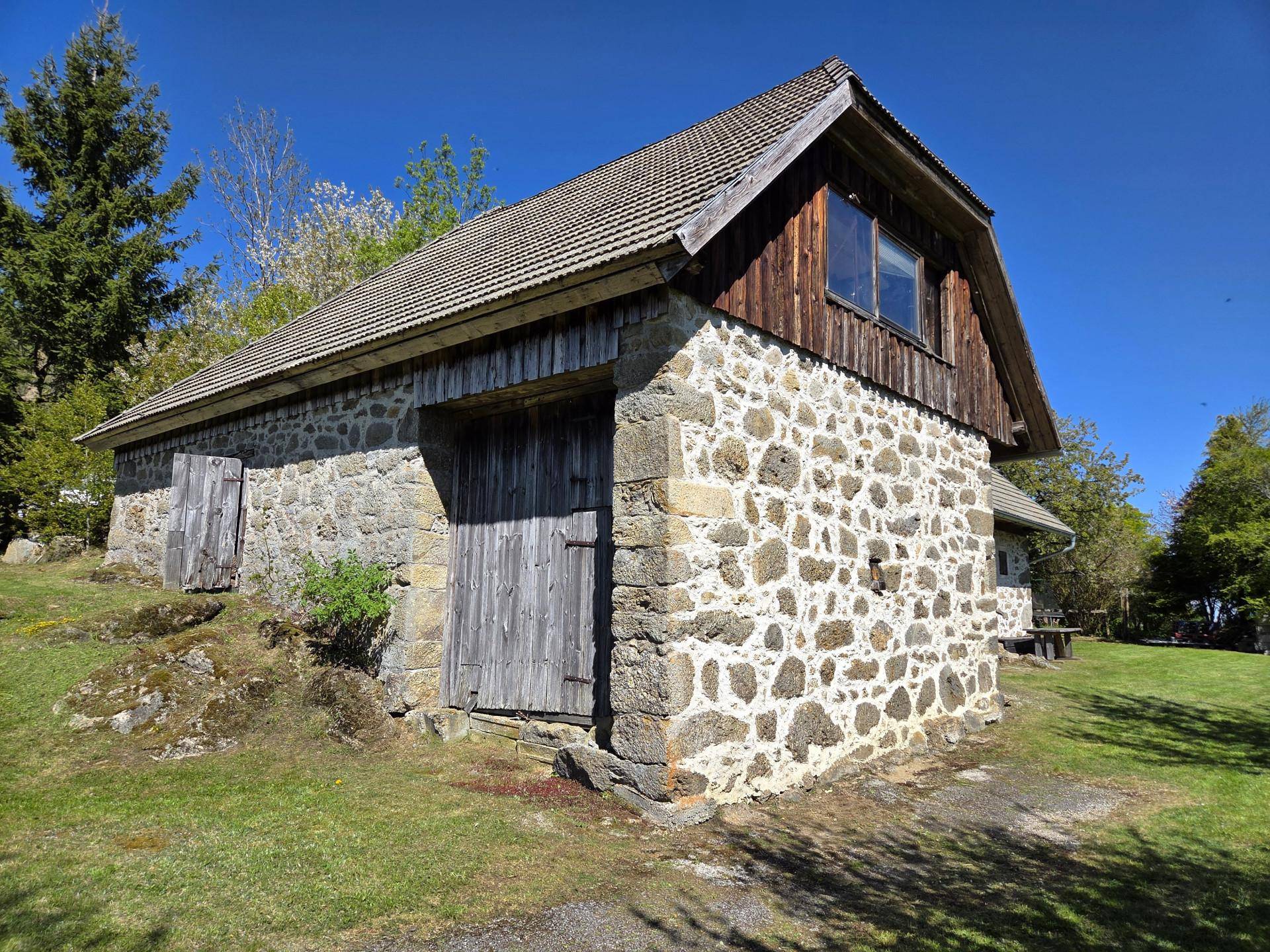 Rustikales Gebäude mit Steinfassade und Holzelementen, umgeben von grüner Natur.