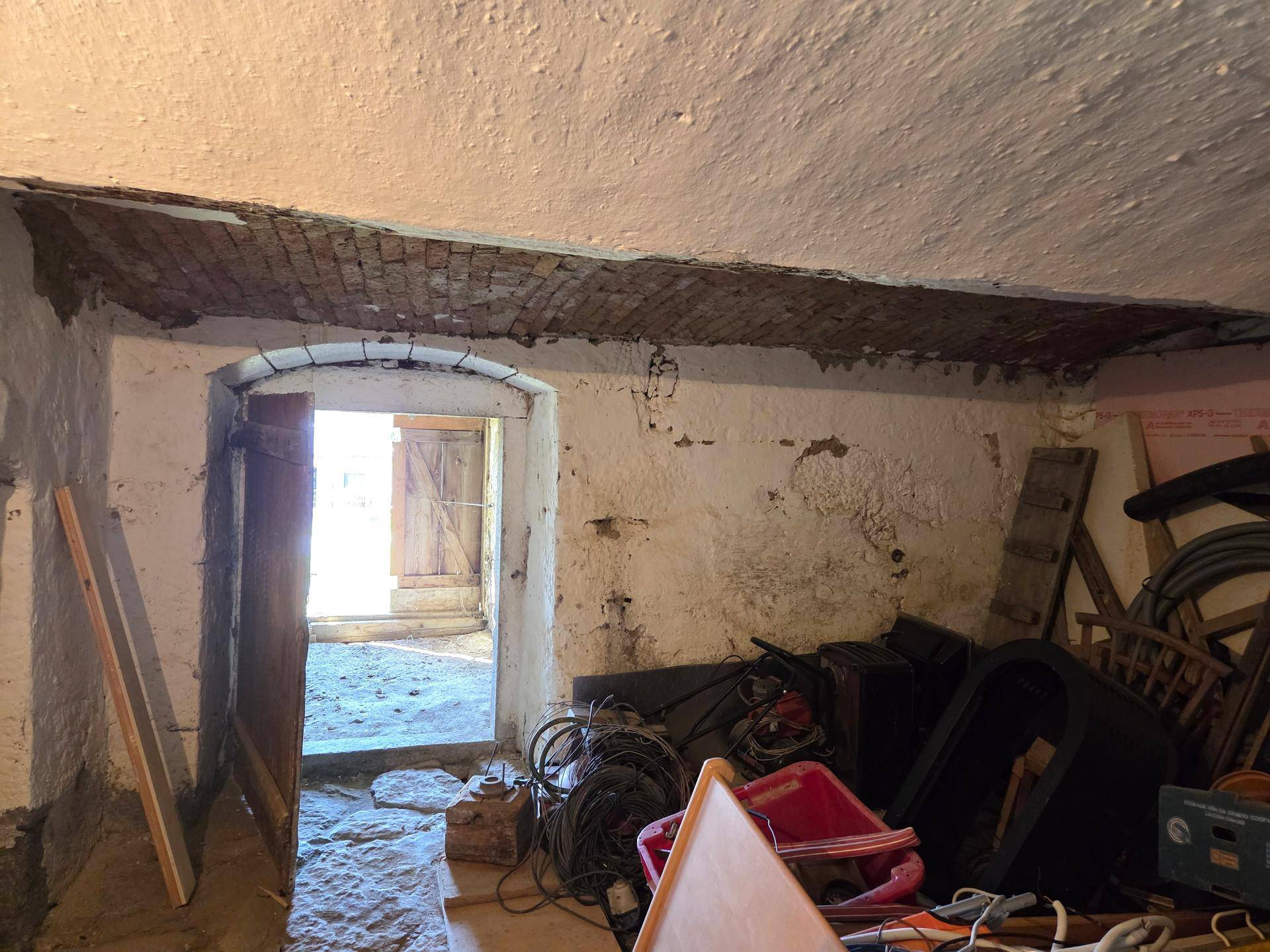 Kellerraum mit unverputzten Wänden und gewölbtem Durchgang, ideal als Lagerfläche oder Werkstatt.