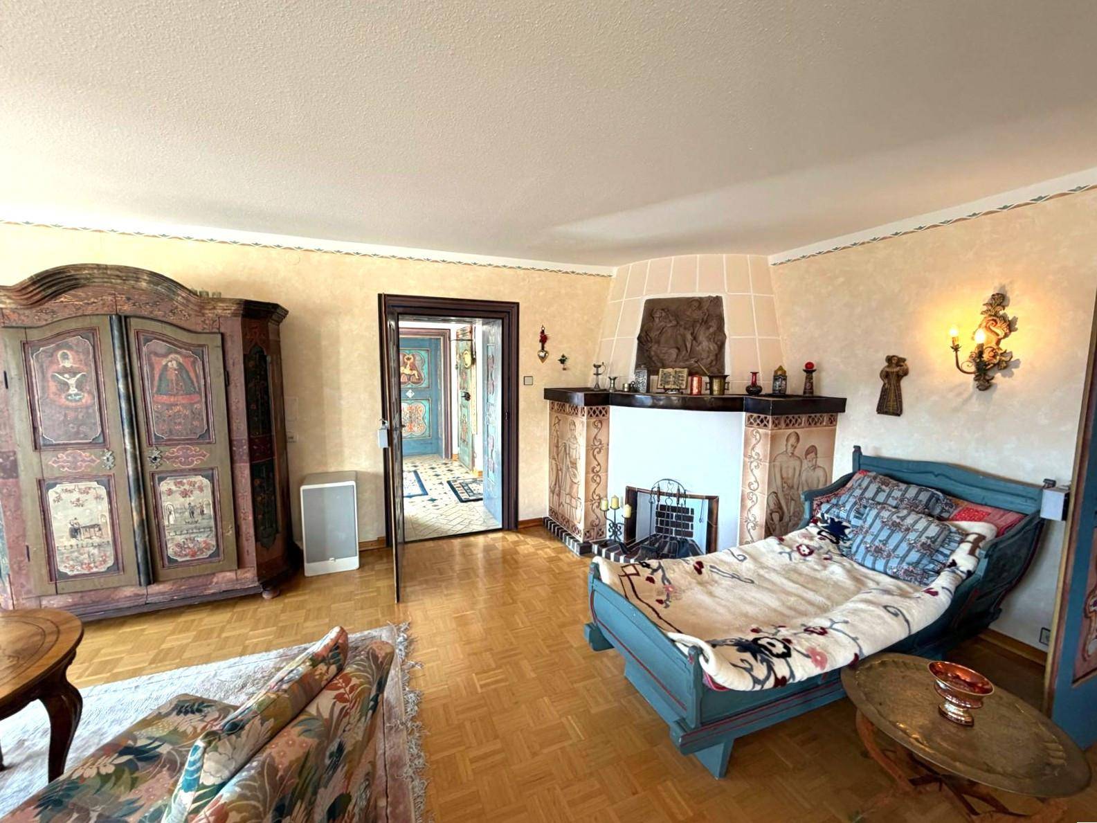 Wohnzimmer mit kunstvoll bemaltem Schrank, traditionellem Kachelofen und rustikalem Tagesbett.