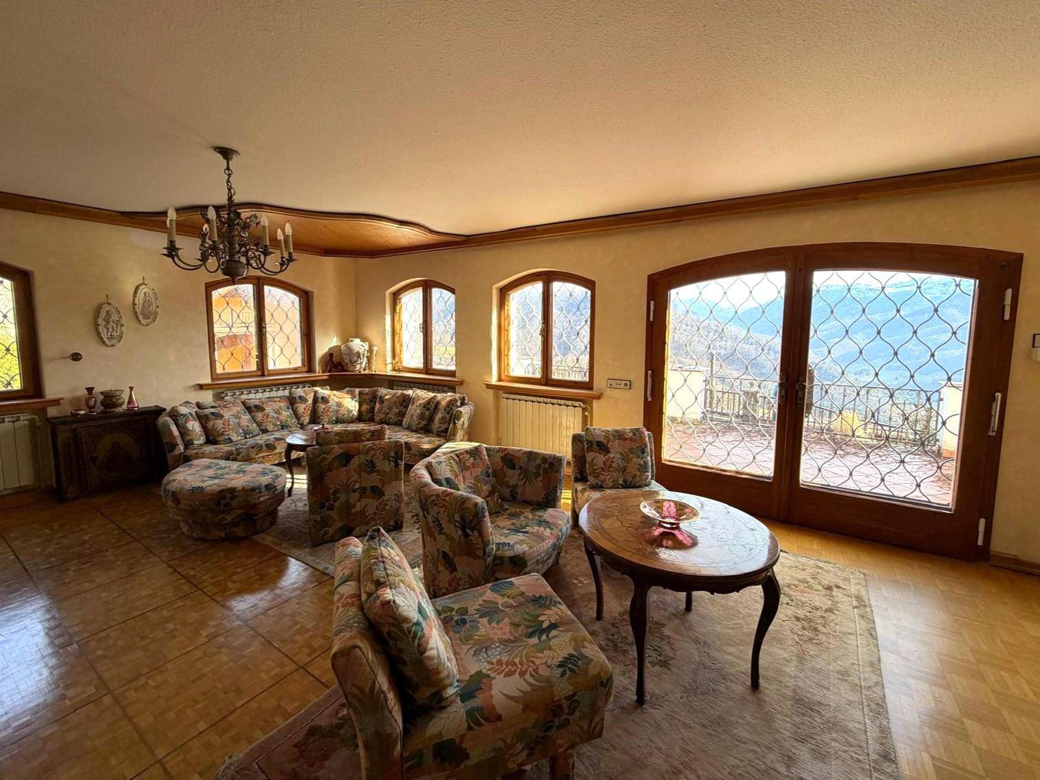 Helles Wohnzimmer mit gemütlichen Sitzgelegenheiten, Holzboden und Zugang zu einem Balkon mit Weitblick.