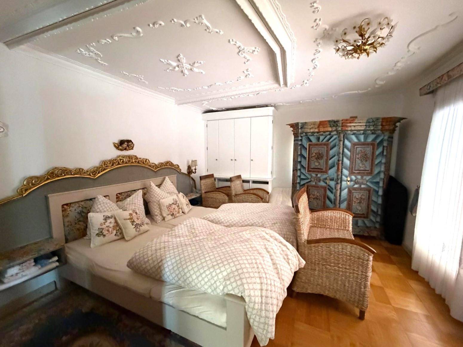 Geräumiges Schlafzimmer mit großem Bett, Stuckdecke und einem weiteren bemalten Kleiderschrank.