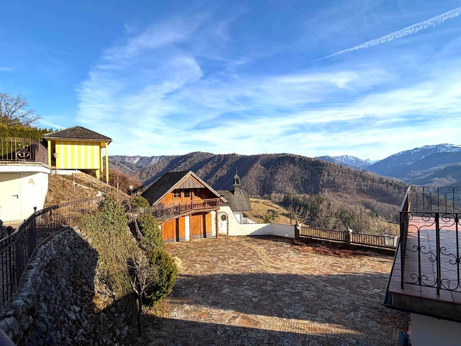 Außenbereich mit gepflastertem Hof, Nebengebäuden und weitem Blick auf die umliegende Berglandschaft.