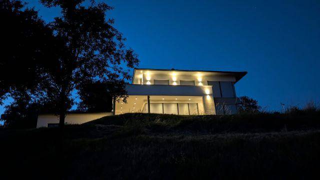 Modernes Haus auf einem Hügel bei Nacht, stimmungsvoll beleuchtet von Außenleuchten.