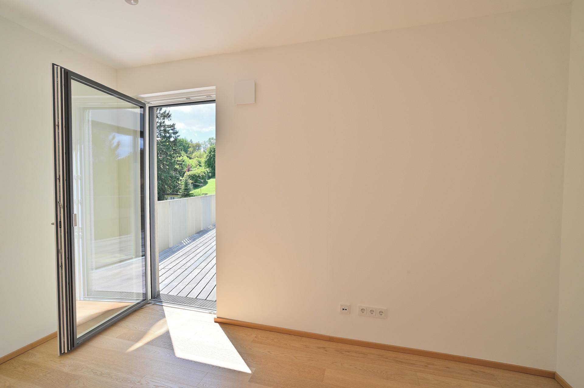 Helles Arbeitszimmer mit Holzboden und Zugang zu einem Balkon mit Blick ins Grüne.