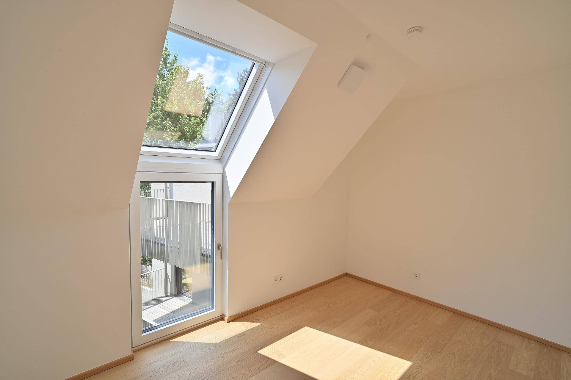 Helles Schlafzimmer mit Dachfenster, Holzboden und Zugang zu einem kleinen Balkon.