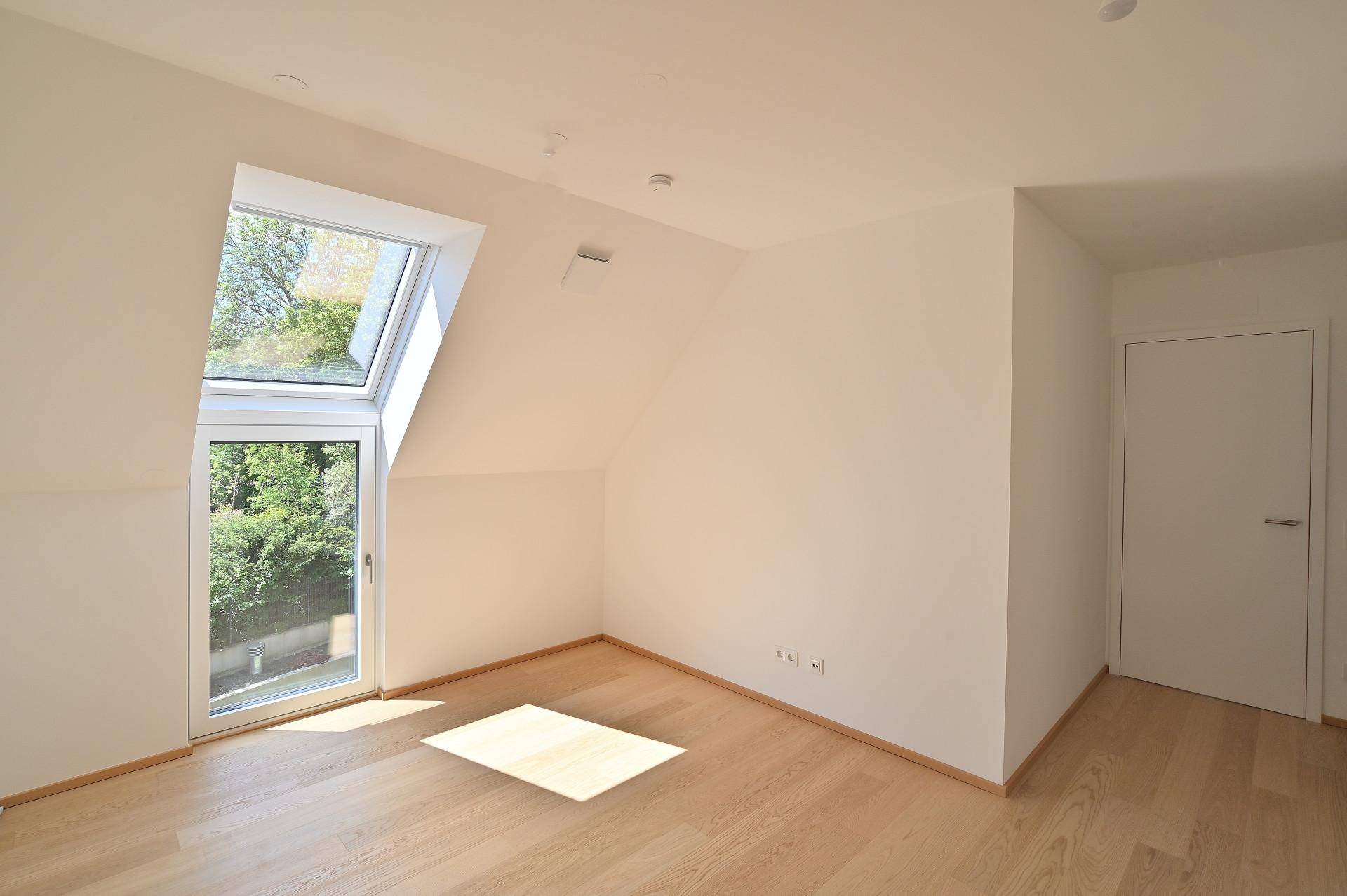 Leeres Schlafzimmer mit Holzboden, Dachfenster und Blick ins Grüne.