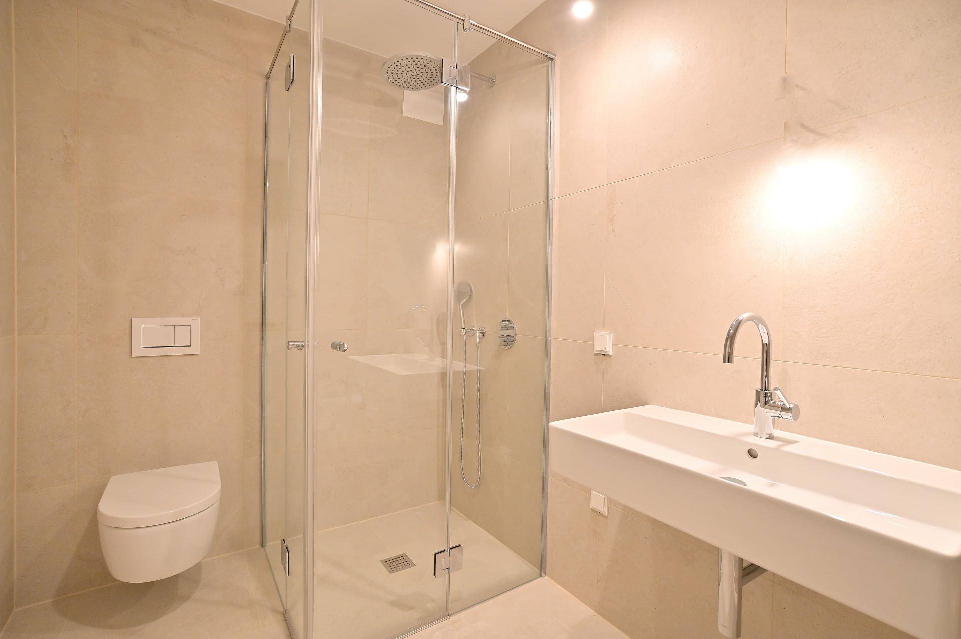 Modernes Badezimmer mit beigefarbenen Fliesen, Dusche, WC und Waschbecken.